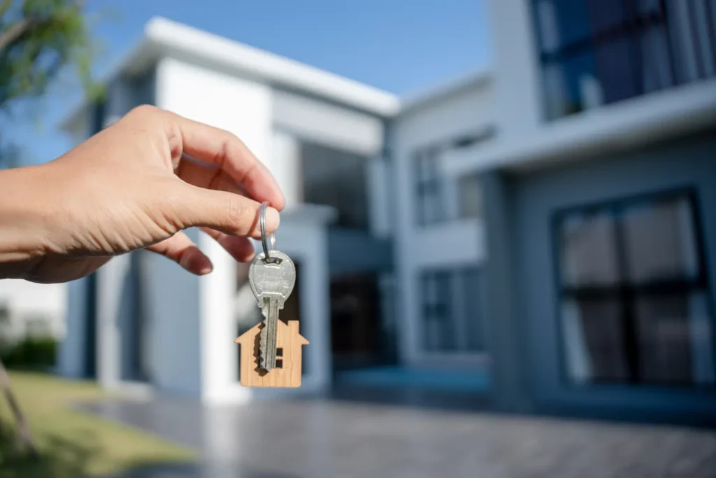 Rental property software depicted by a hand holding house-shaped keys in front of a modern home.