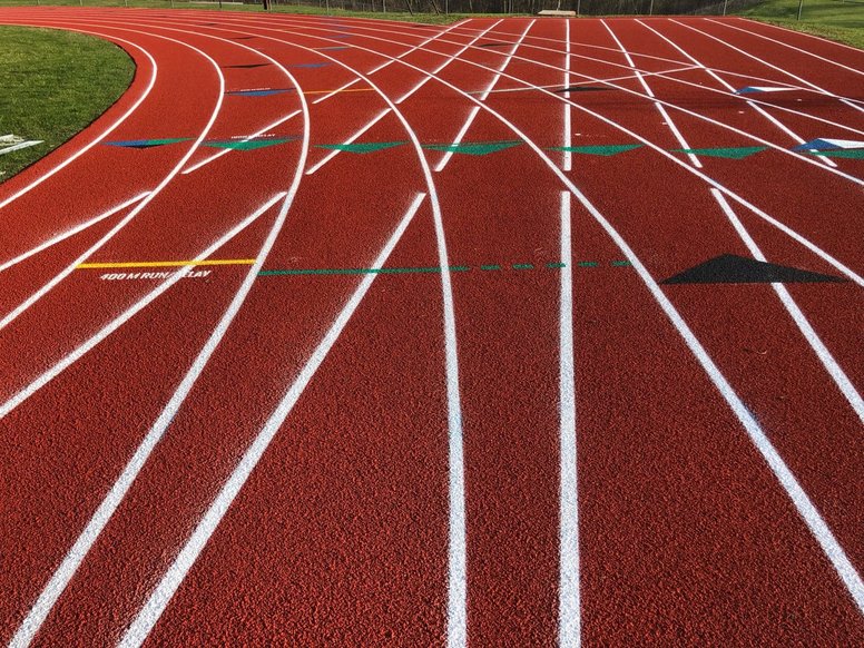 Running track construction showing a completed red rubber track with precise lane striping, exchange zones, and curved lane geometry.