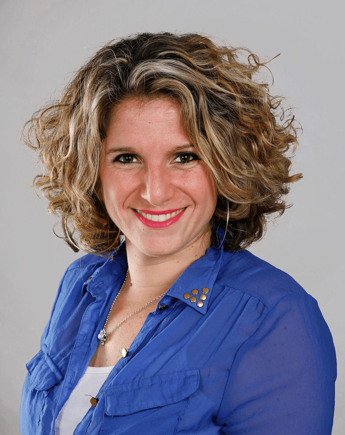Minimal studio portrait of a confident woman in a white shirt, arms crossed, on a soft gray background.
