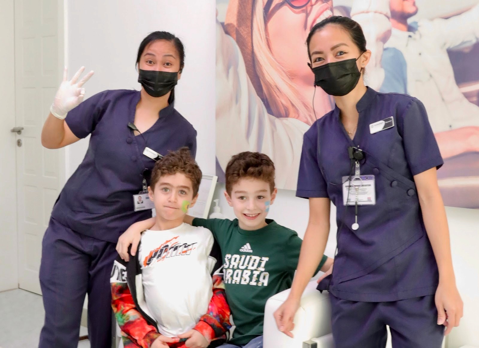 طفلان مع طبيبتا أسنان أطفال في عيادة أطفال مركز إنفزلاين لطب الأسنان، يبتسم الأطفال بسعادة بفضل تعامل أطباء أسنان الأطفال المريح والمطمئن معهم.