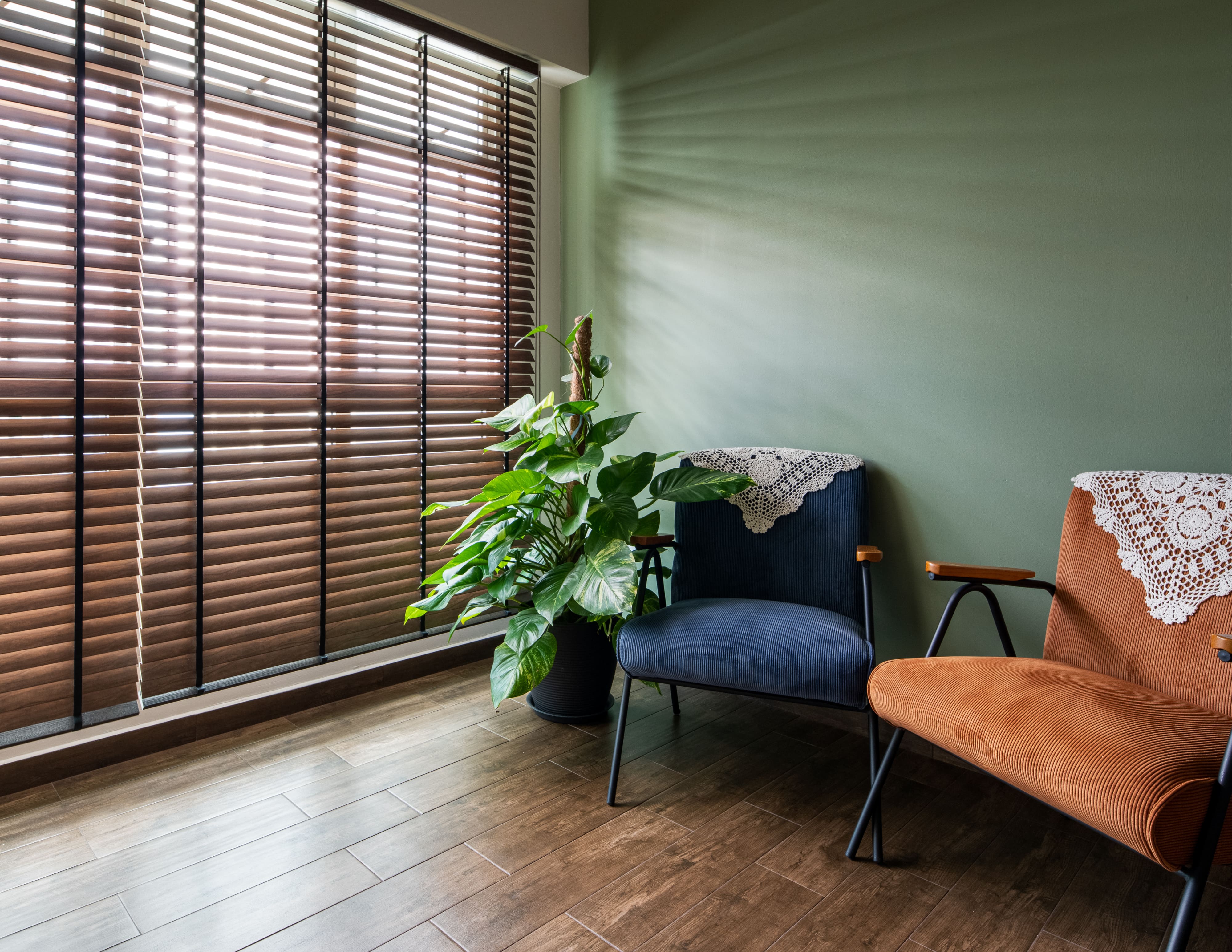 Relaxation corner with retro-inspired seating, greenery, and wooden blinds, designed to bring warmth and calm to the home.