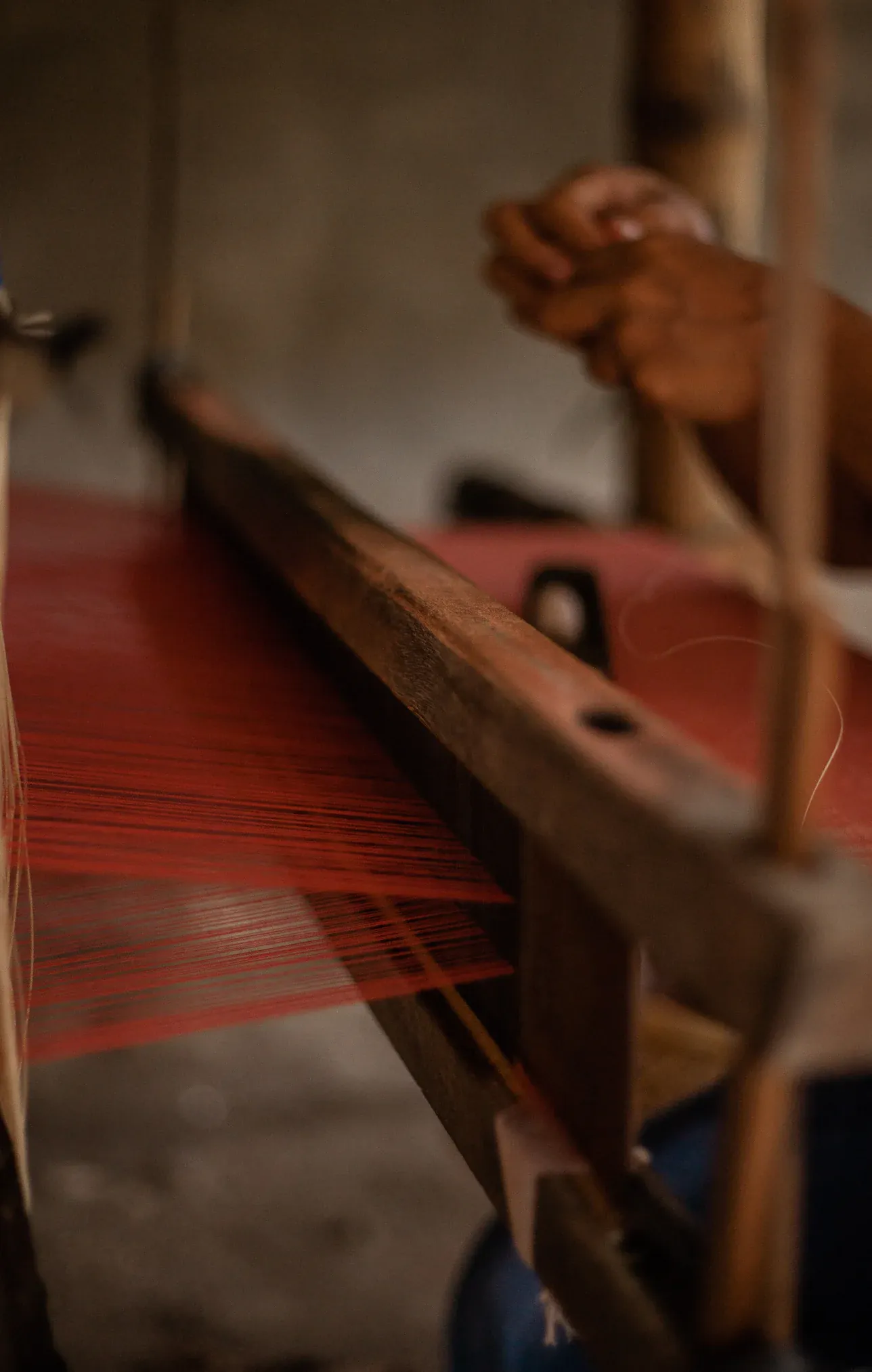 A weaver at a wooden loom strung with red thread in Argao, Cebu, Philippines
