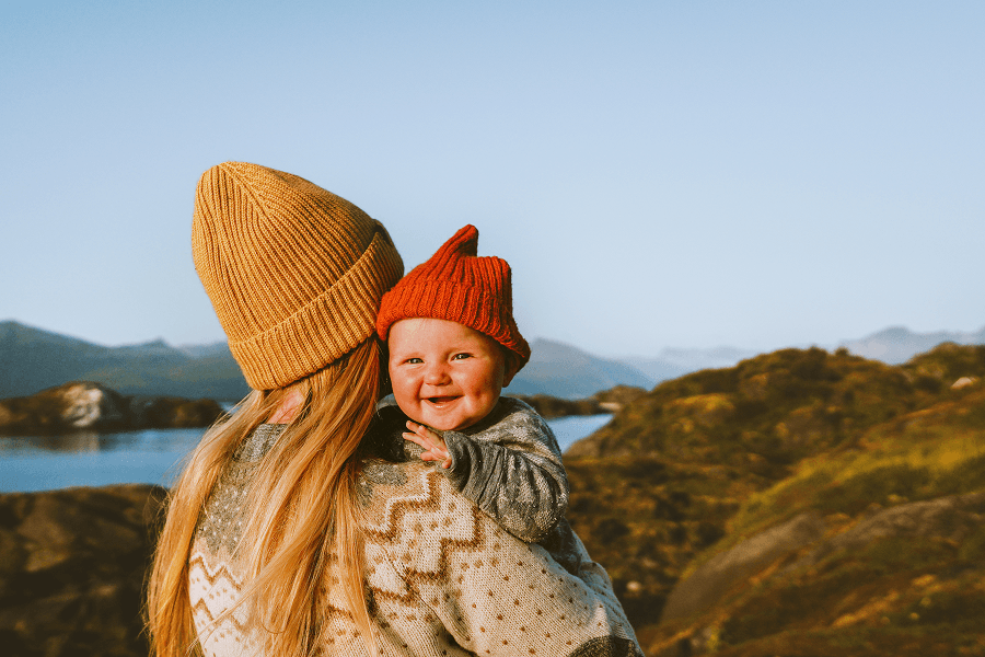 Pregnant person in a yellow coat holding a laughing toddler outdoors