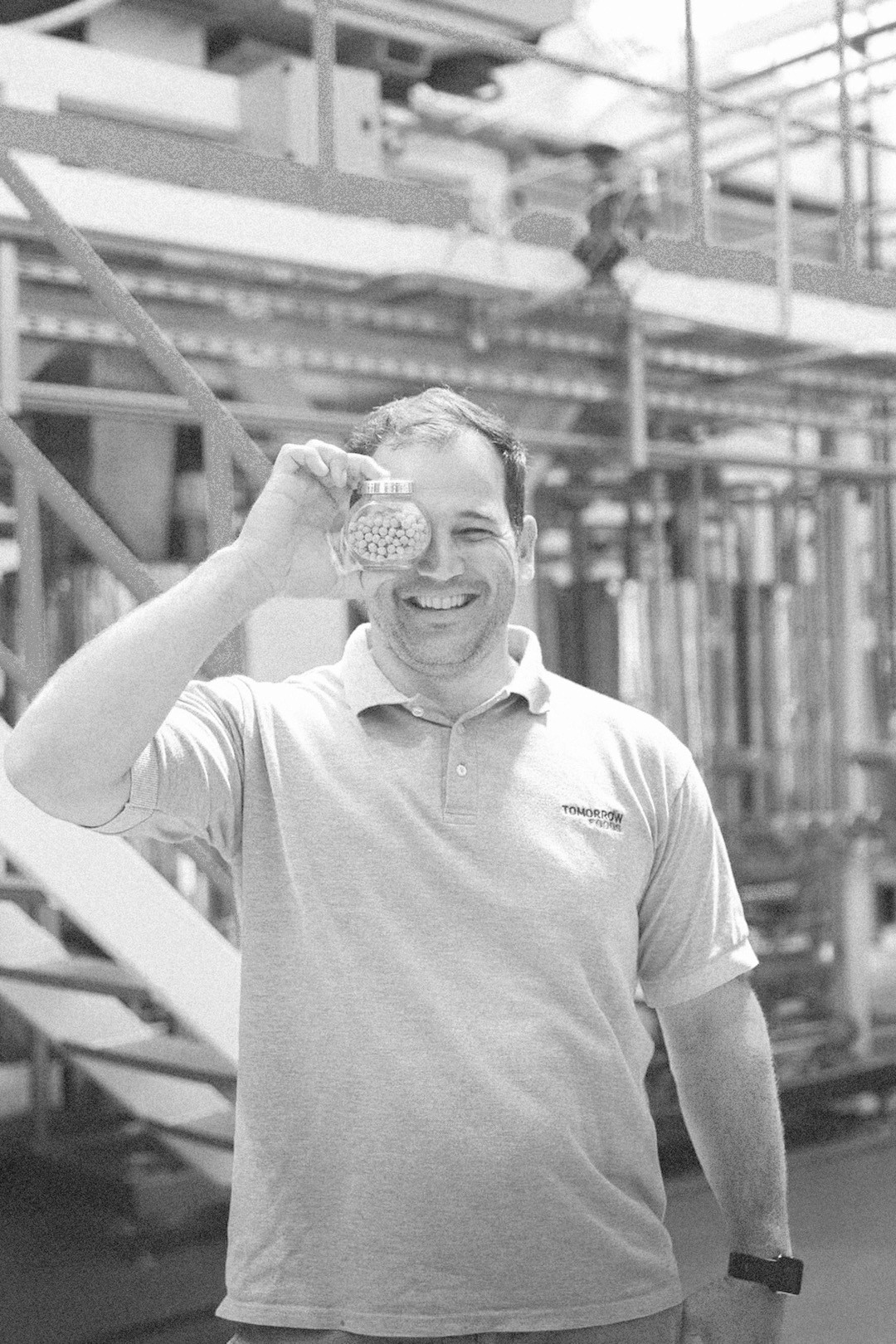 Individual holding a glass container in an industrial setting, wearing a “Tomorrow Water” shirt.