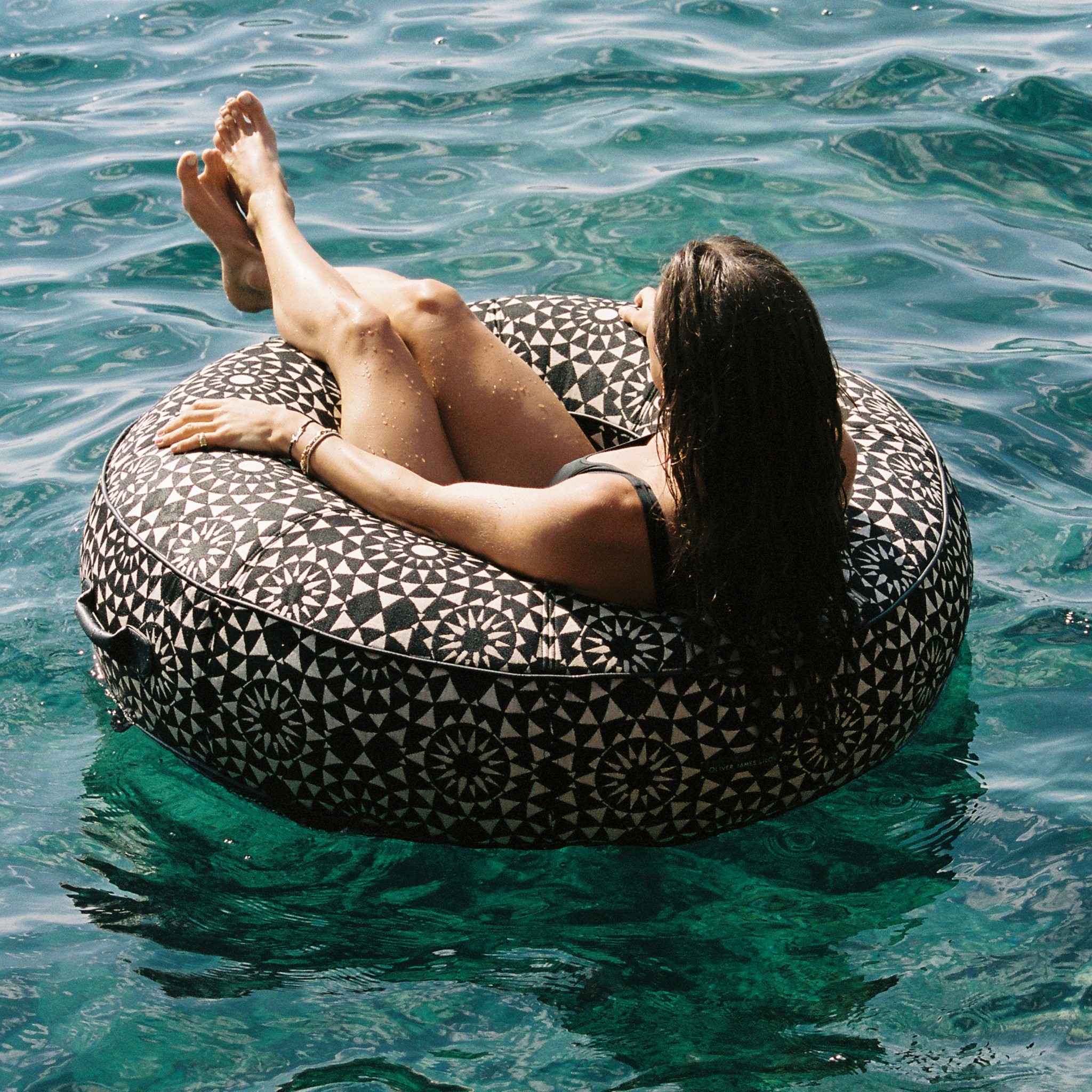 Woman floating in a luxury black-and-white geometric ring pool float in crystal-clear sea