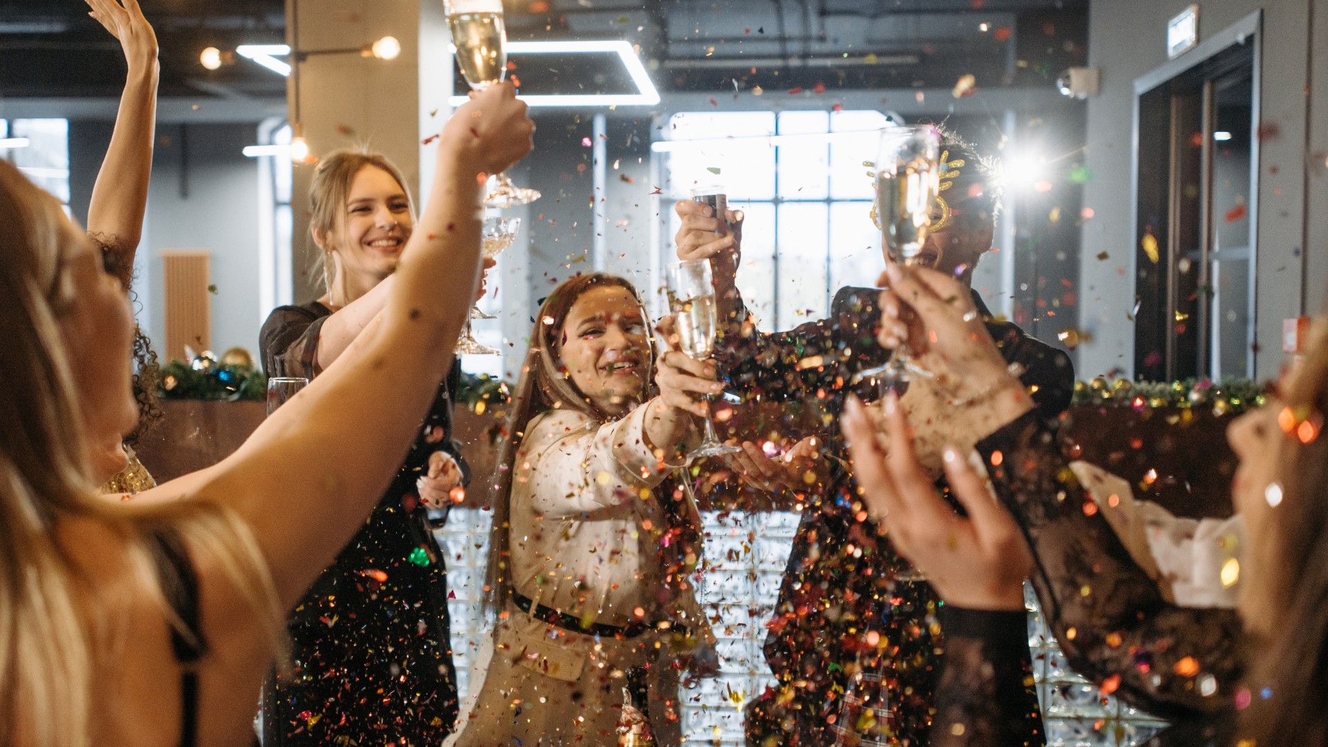 eine gruppe von menschen feiert etwas in einer art büro-raum, sie trinken champagner und es ist sehr viel glitzer in der luft