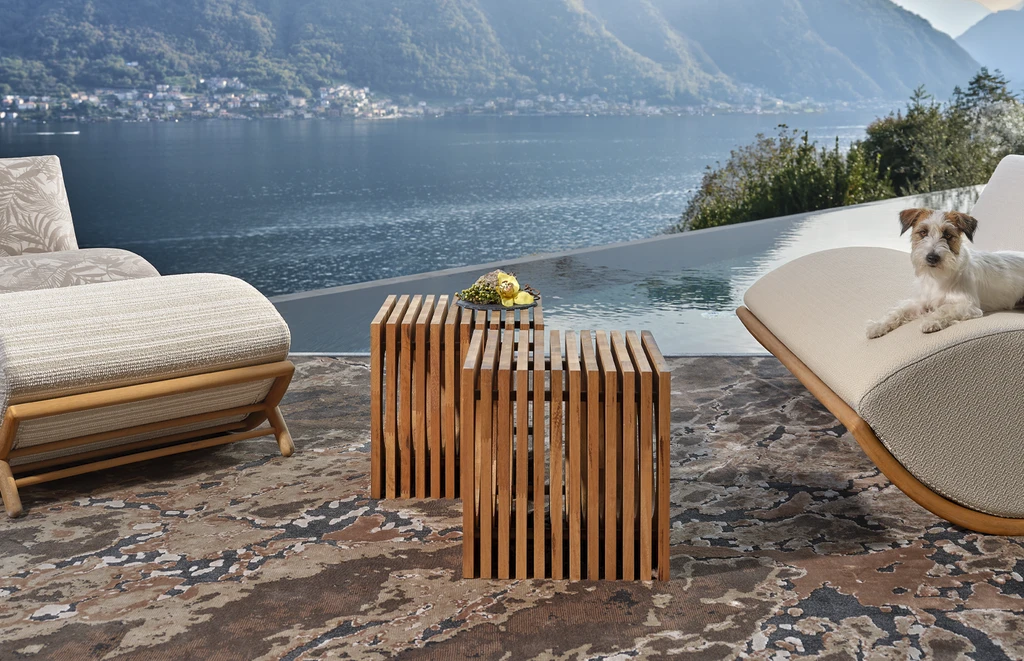Luxury outdoor side table in solid Iroko wood, featuring vertical slats and a sculptural cylindrical shape, lake como modern villa view.