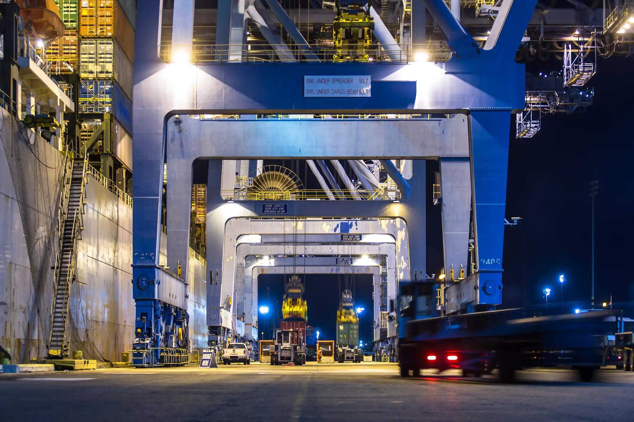 Steel arch bridge lit with blue lights at dusk, with cars and trucks crossing over a river.