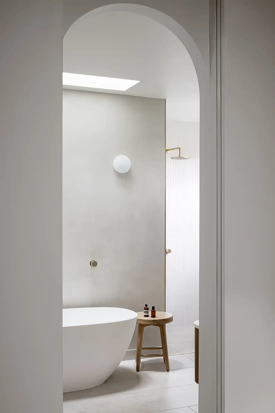 A white bathroom with a freestanding bathtub visible through an archway