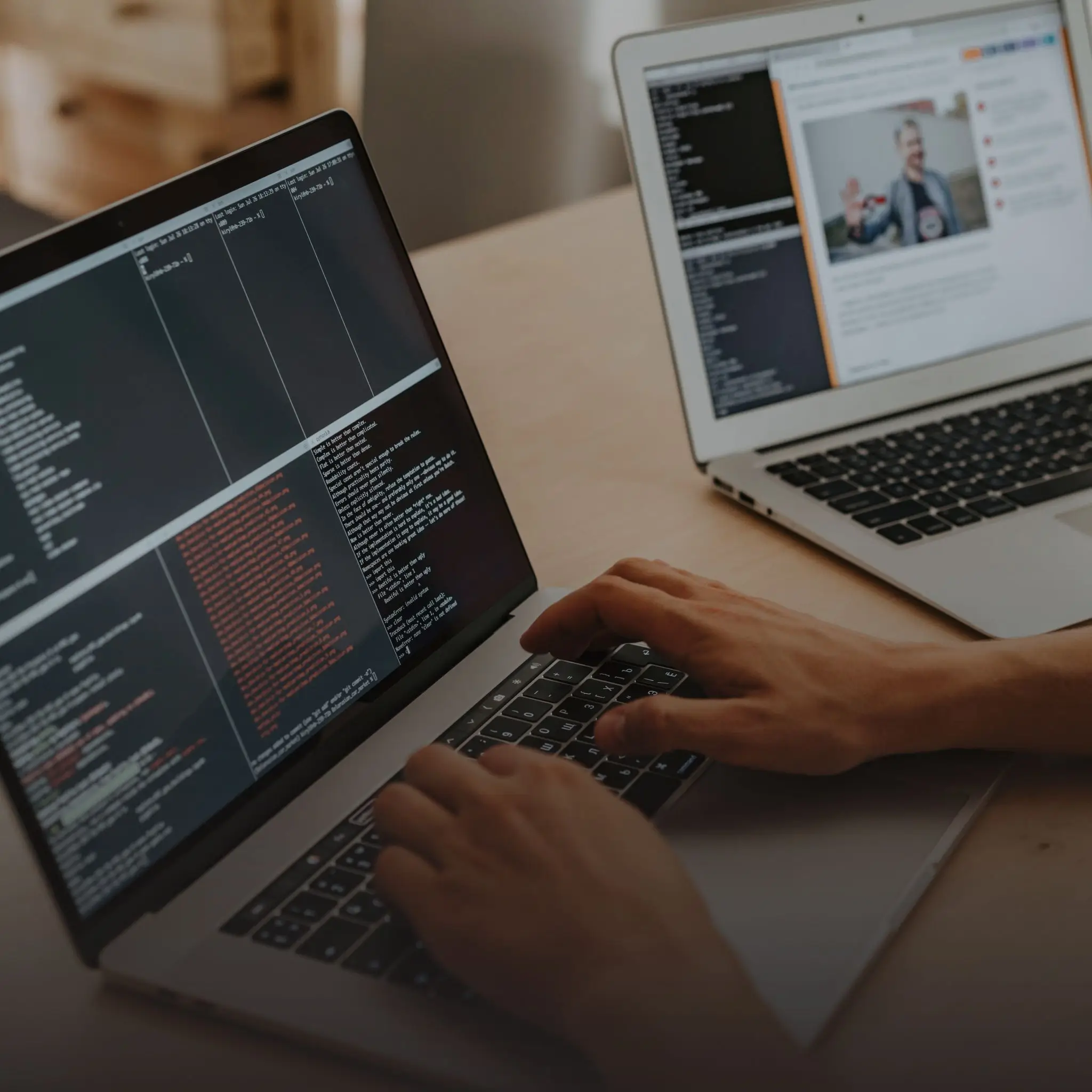 Een persoon typt code op een laptop terwijl een andere laptop in de achtergrond een website met een artikel en foto weergeeft.
