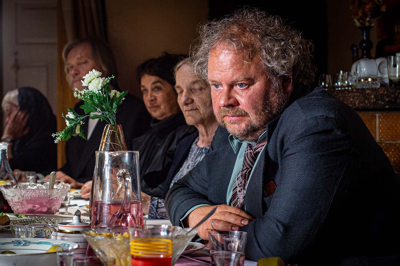 Scene from Estonian Funeral, showing a man drinking during a chaotic family gathering. A dark comedy about love, identity, and clashing generations in modern and traditional Estonia.