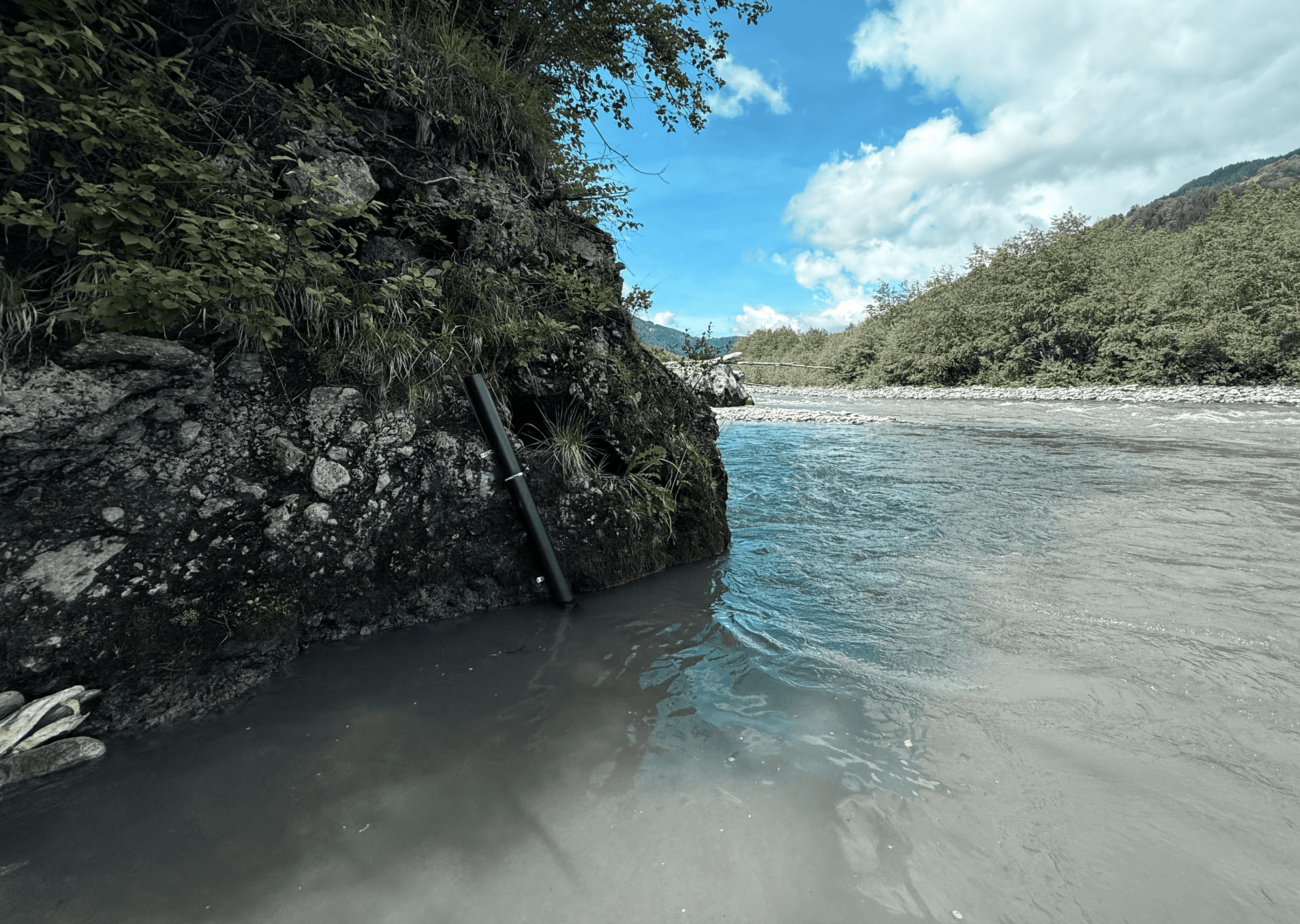 Sensor placed along a riverbank measuring freshwater conditions in a natural landscape.