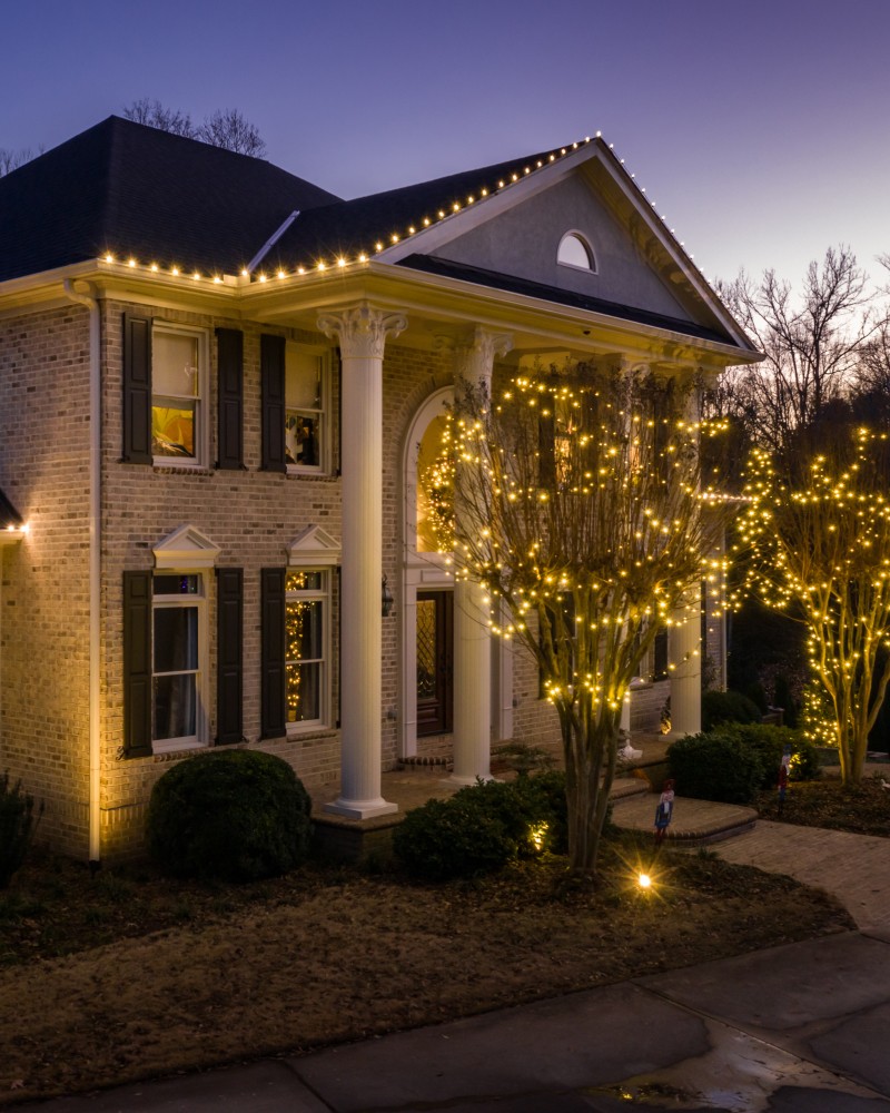 A smiling young man with crossed arms, wearing a plaid shirt and white t-shirt, poses against a dark background.