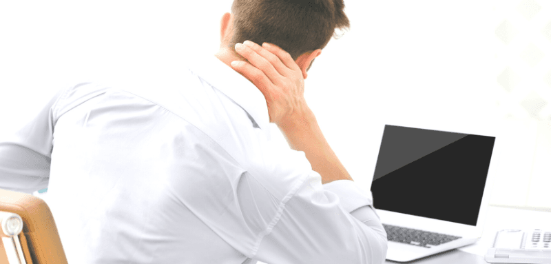 rear view of man sitting in front of laptop with hand on back of neck