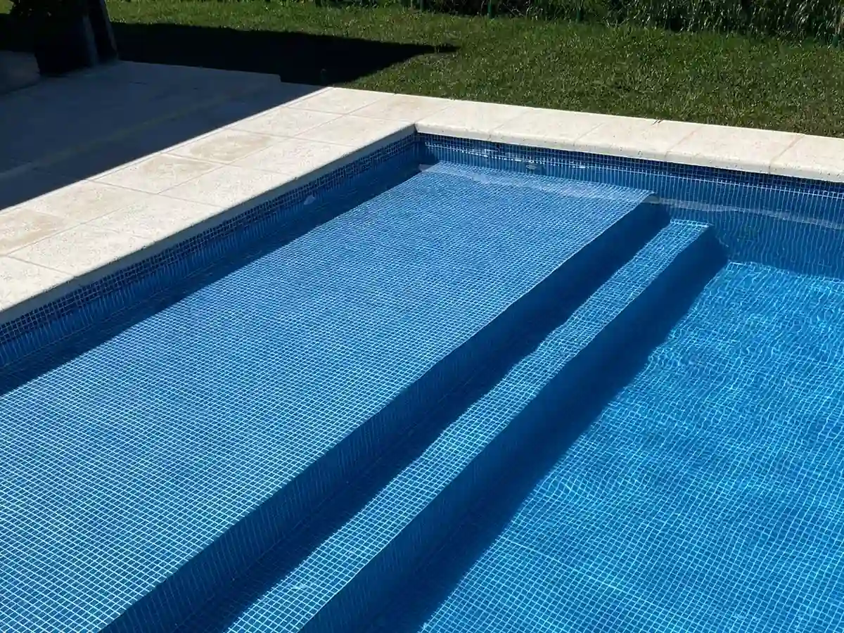 Pileta de hormigón armado con escalones amplios y minimalistas, revestida en venecitas color azul profundo brillante bajo el sol.