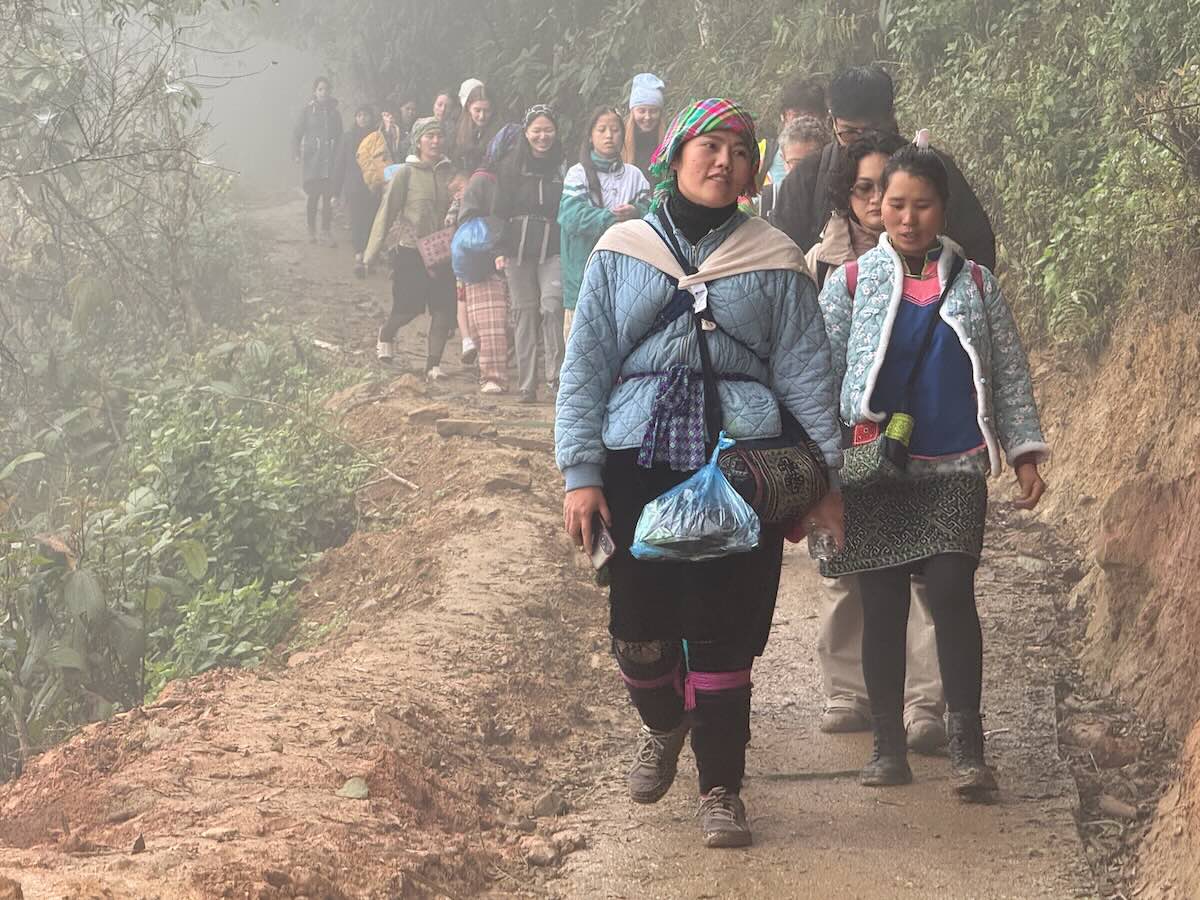 Local Hmong women and hikers walking together along a misty mountain trail near Sapa.