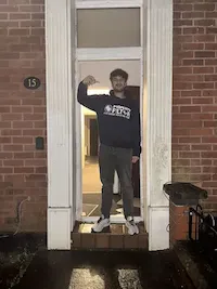 Person standing in the doorway of a brick house holding what appears to be keys