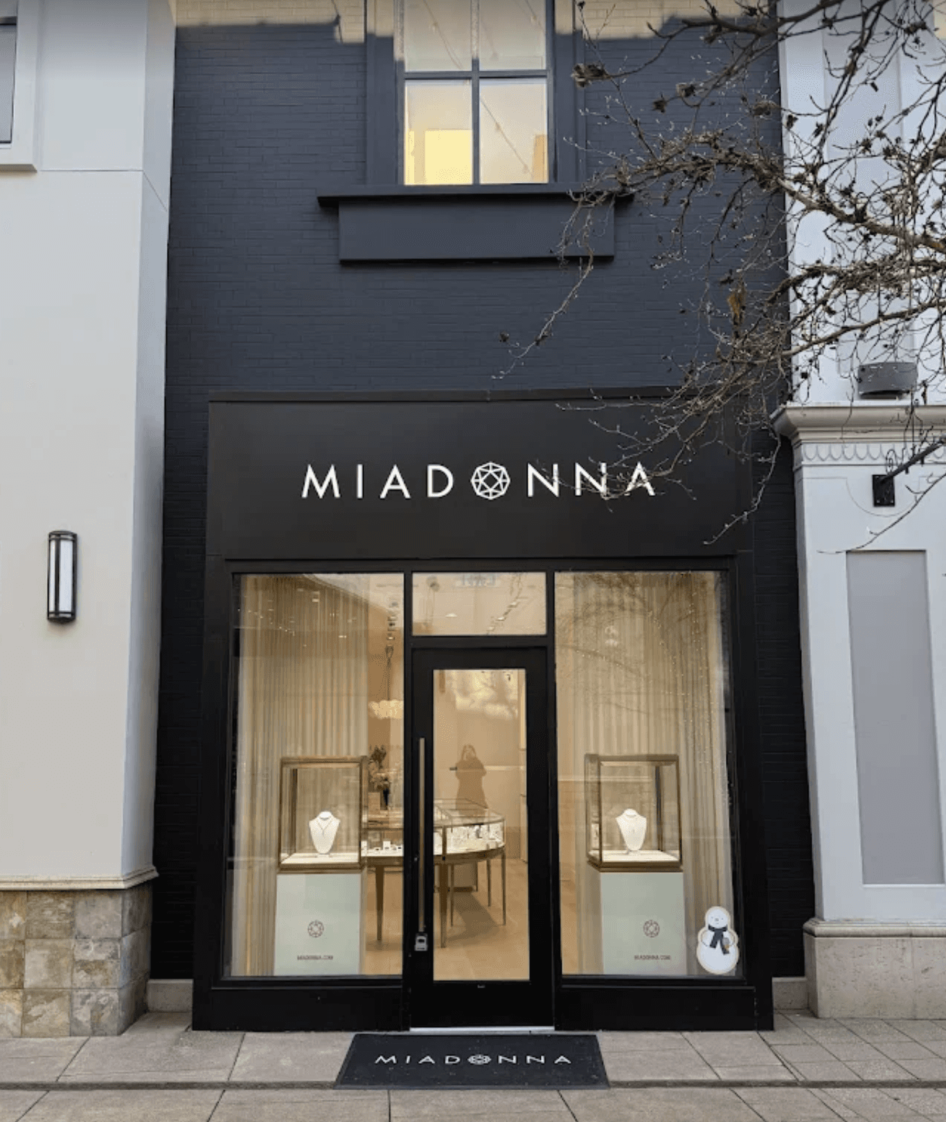 MIADONNA storefront with illuminated brand signage above a black retail entrance and large display windows showcasing jewelry displays.