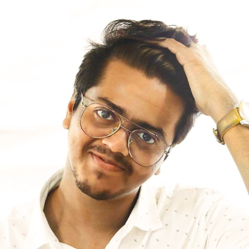 The image features a close-up portrait of a person with short, dark hair and round glasses.