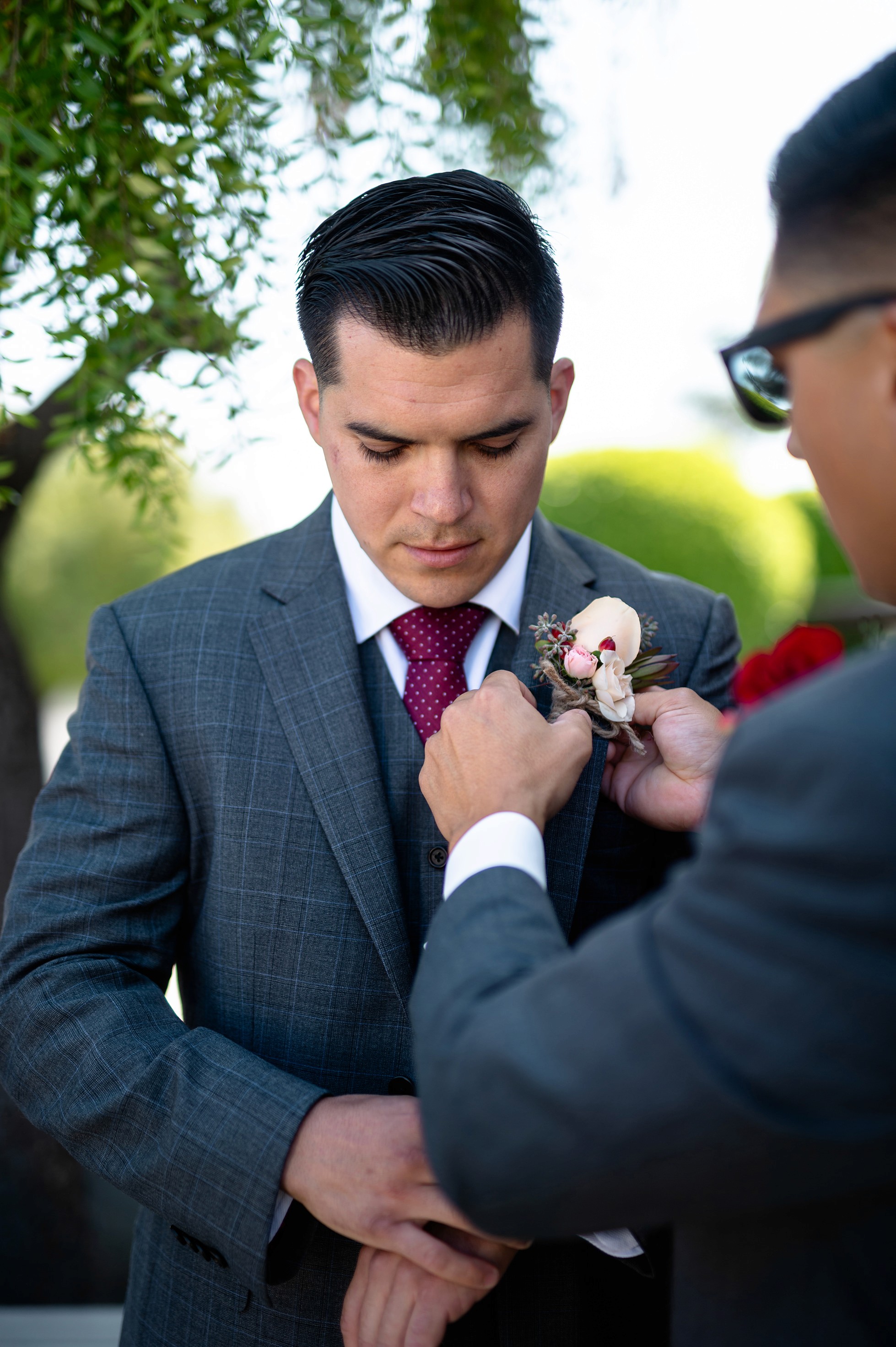 Best man helping groom with boutonniere and tie outside church