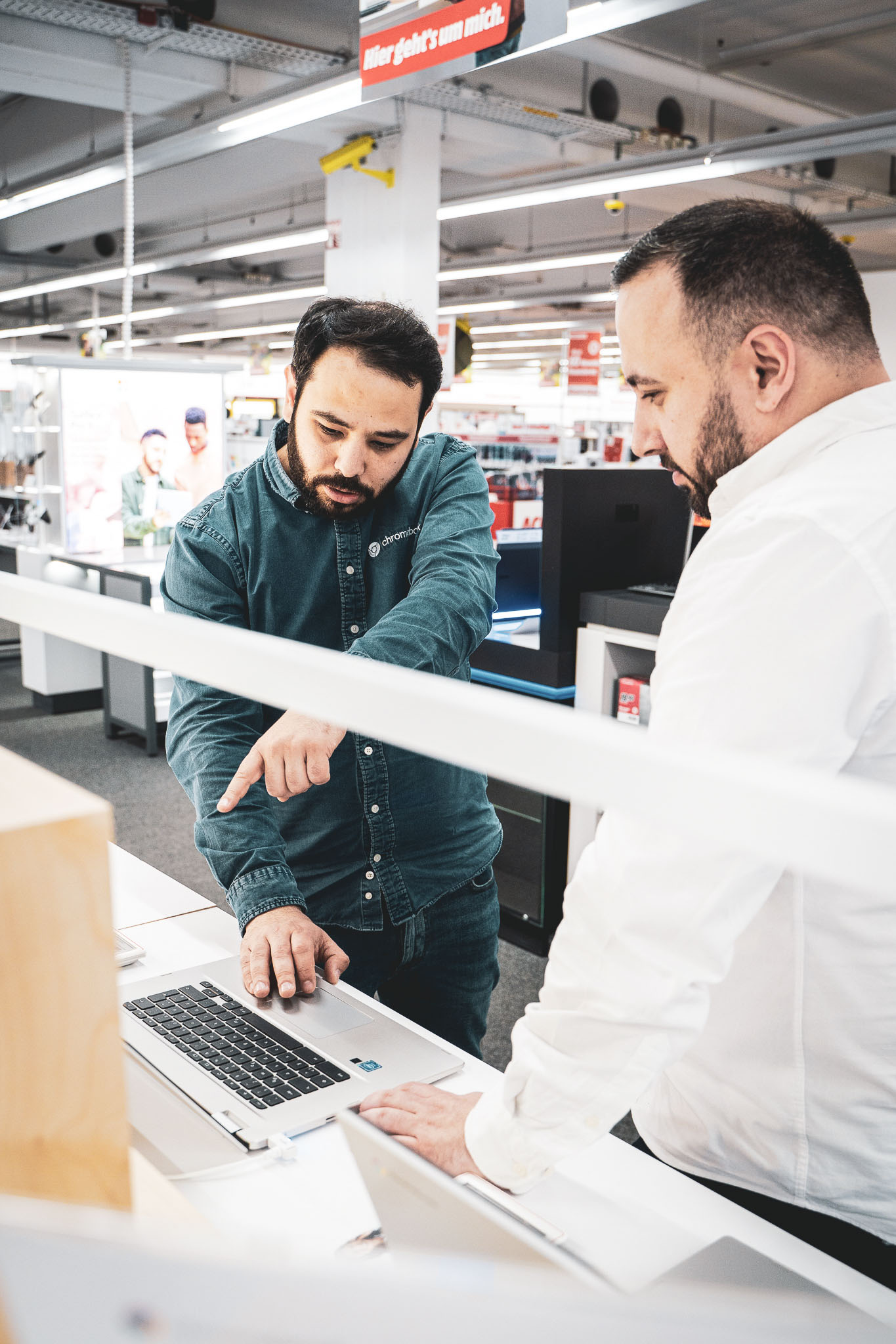 Beratungsgespräch am Verkaufstresen: Ein Promoter erklärt einem Kunden konzentriert ein technisches Produkt. Aktivierung am Point of Sale, bei der Fachwissen und Kundennähe den Unterschied machen.