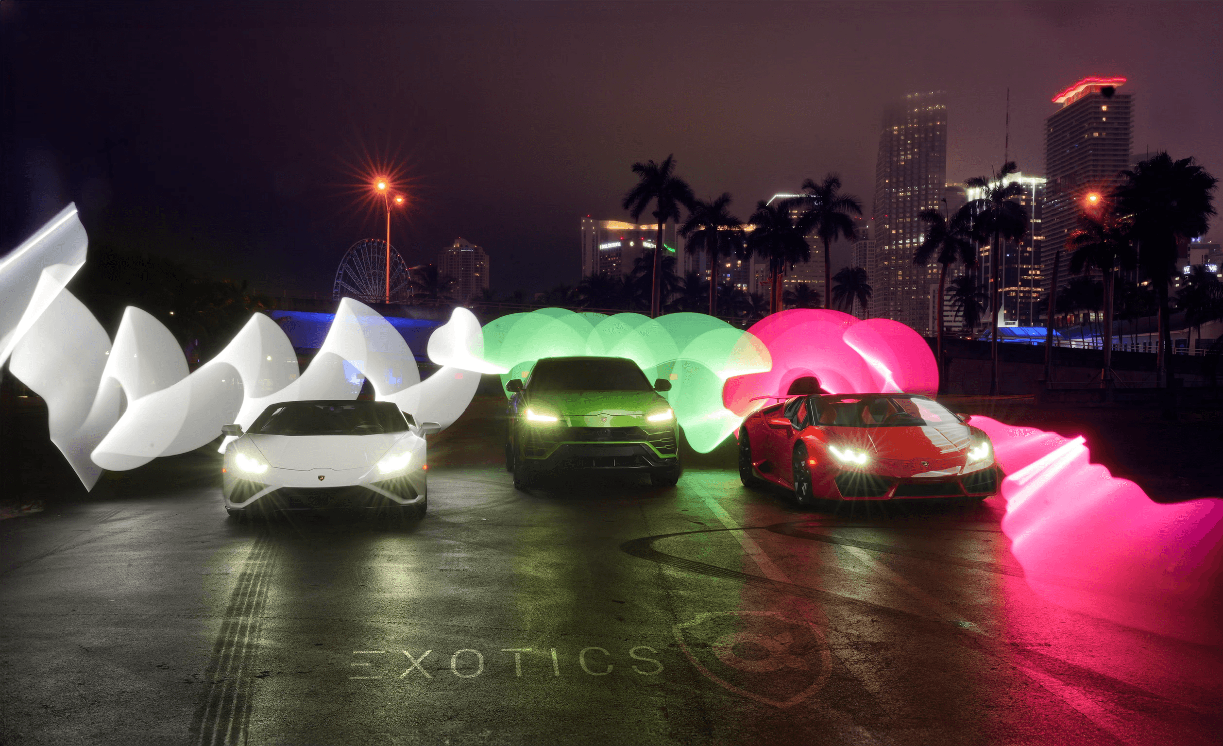 Two people in a workshop, one standing and smiling while the other leans over a car, working on it.