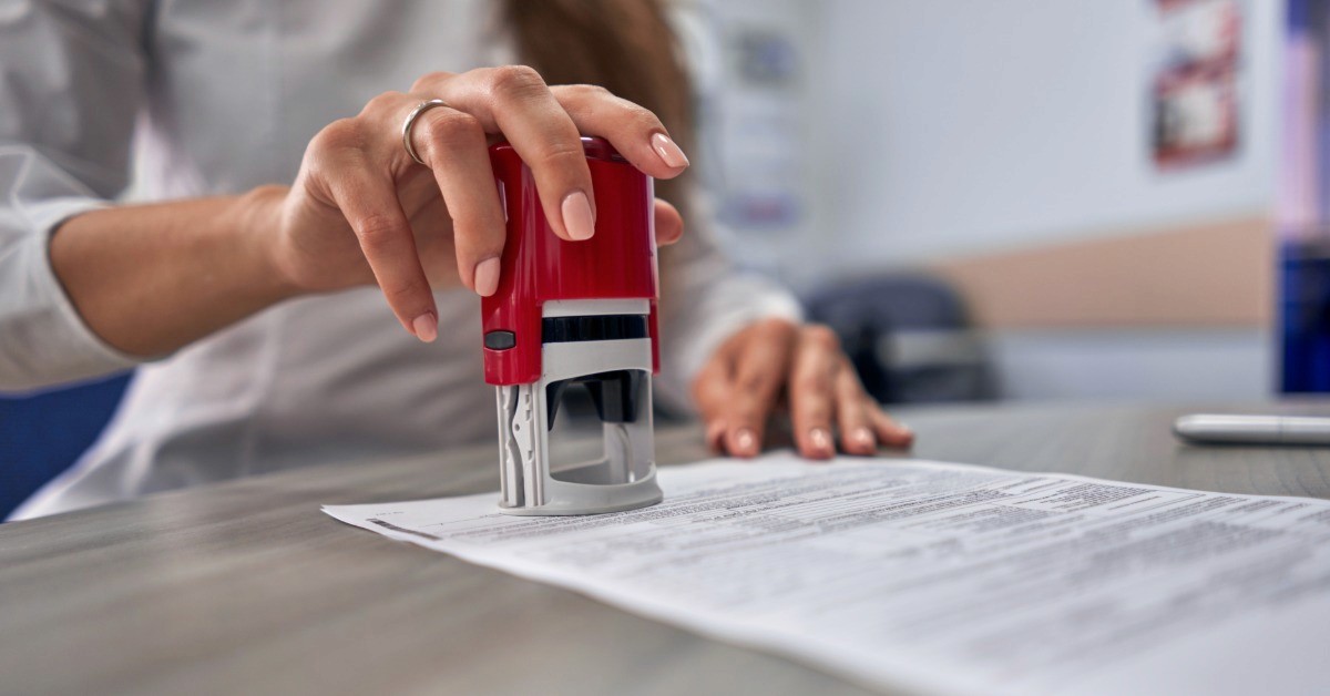 A close-up of someone typing on a laptop and holding a pen in the other hand. Digital contract graphics hover over the laptop.