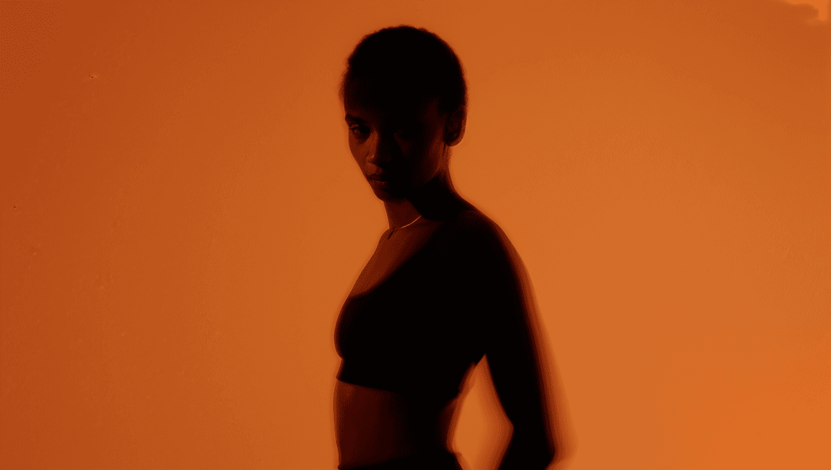 Young woman with short, dark hair and a yellow sweater looks serious, surrounded by hands holding smartphones, conveying intrusion and tension.