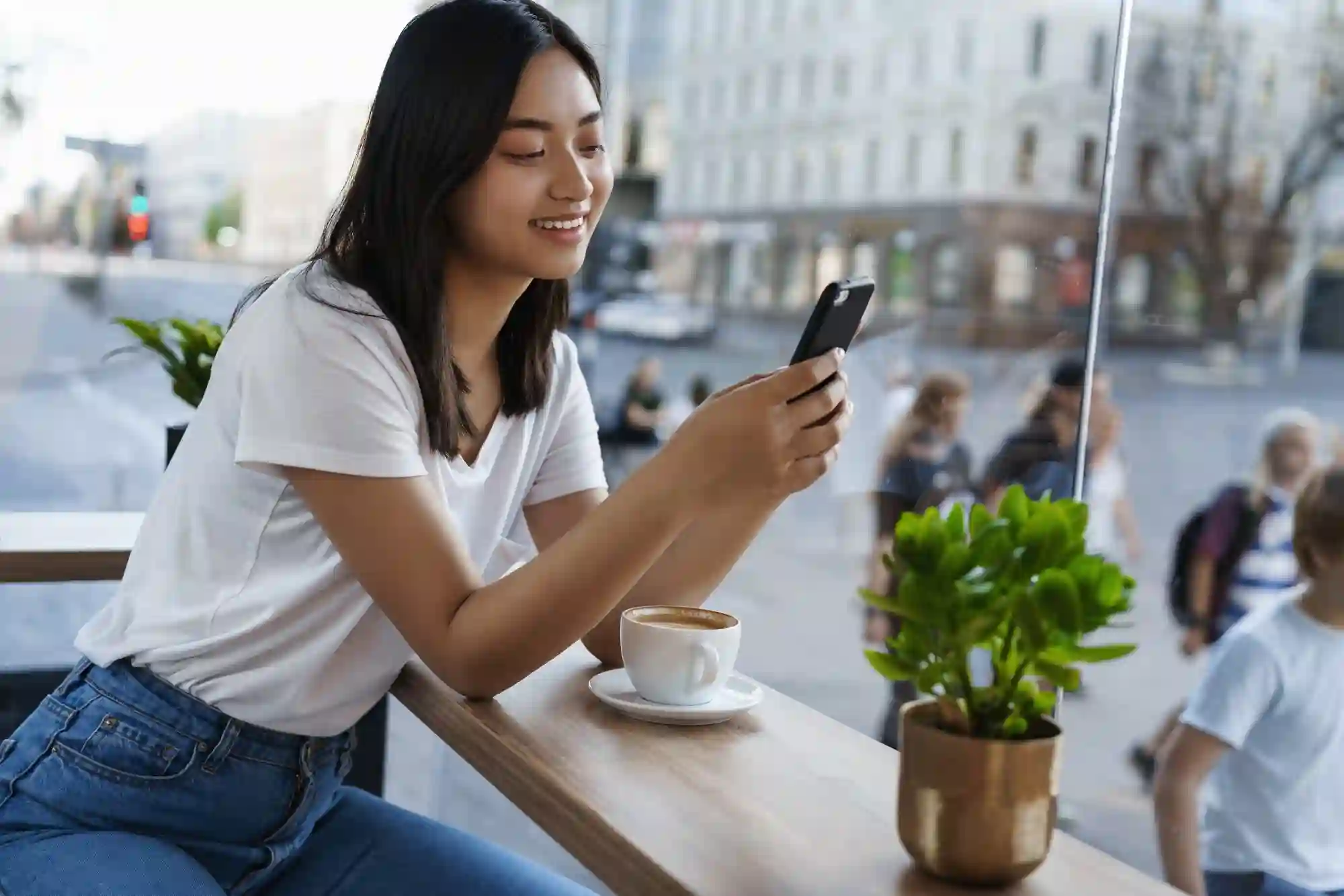 A smiling woman gives a peace sign while her friend captures the moment on a smartphone in a cafe.