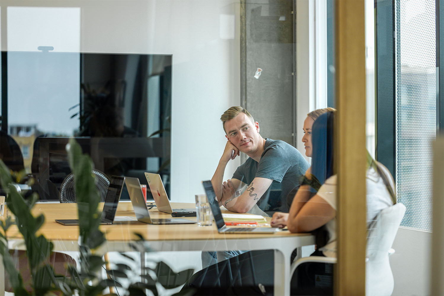 Drie mensen zitten aan een vergadertafel met laptops in een vergaderruimte op kantoor