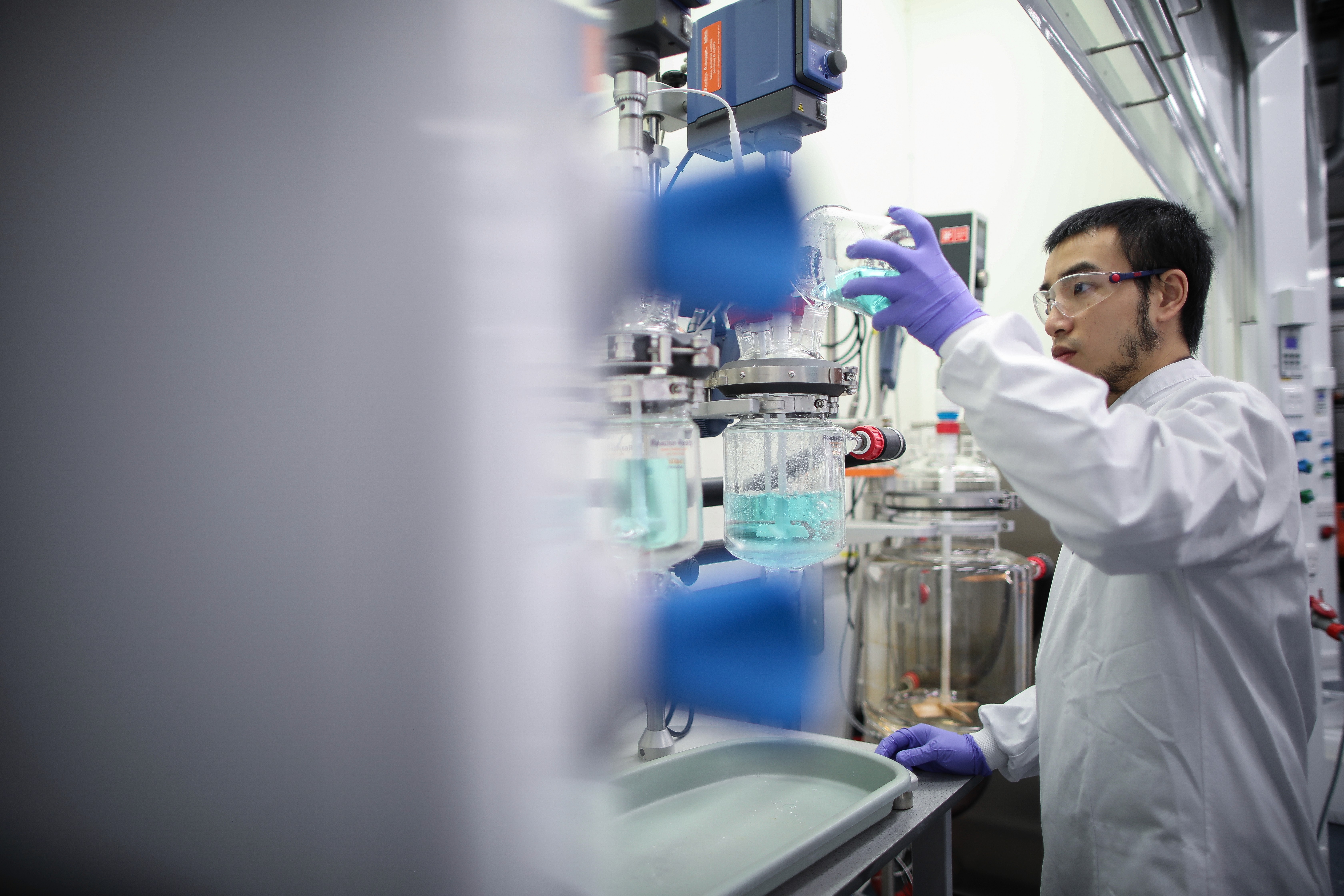 CPI scientist pouring a light blue liquid into a beaker.