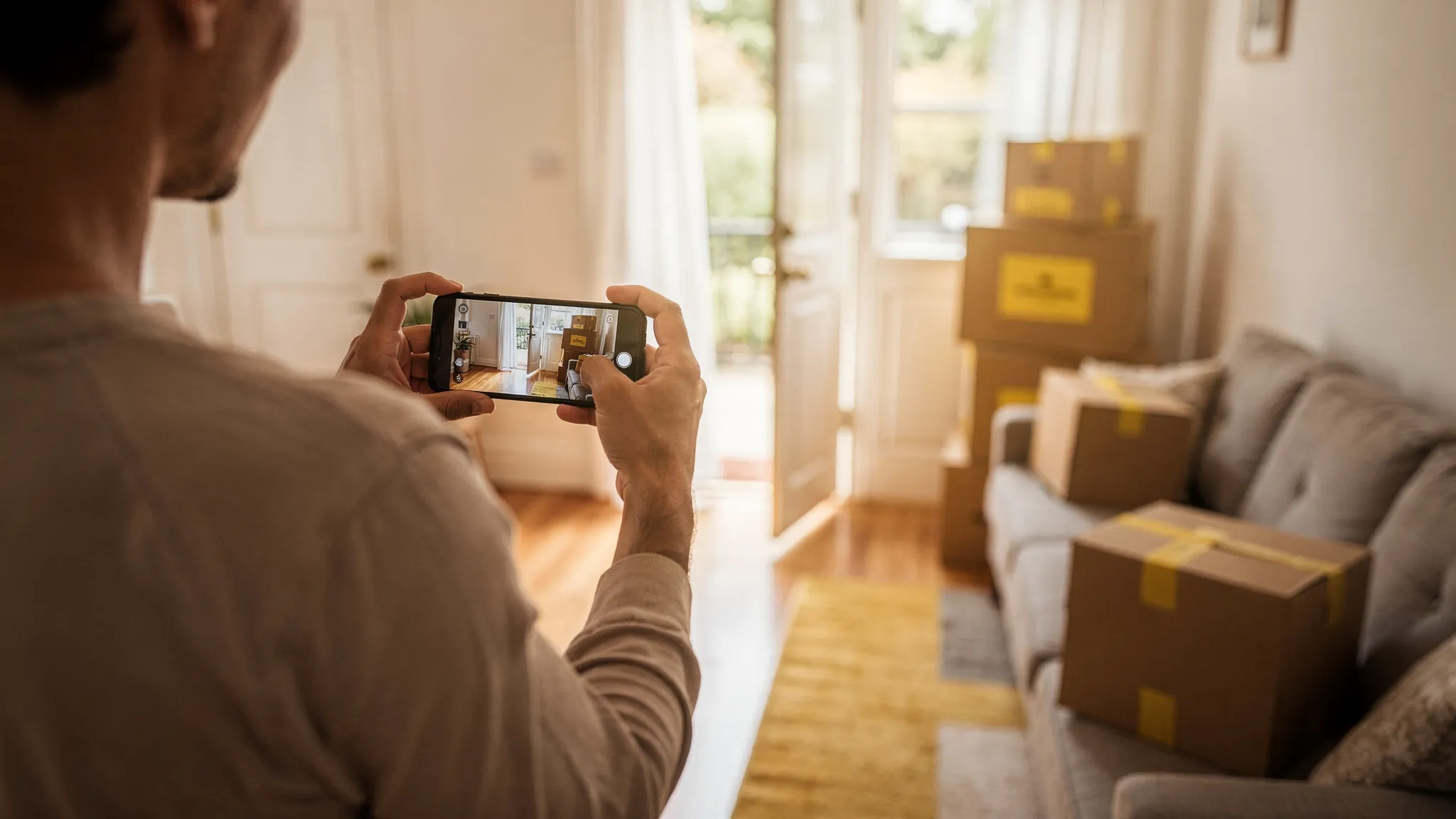 A person using a smartphone to record a quick home walkthrough for a moving quote, showing a living room with a couch, packed boxes, and a clear path to the front door for access assessment.