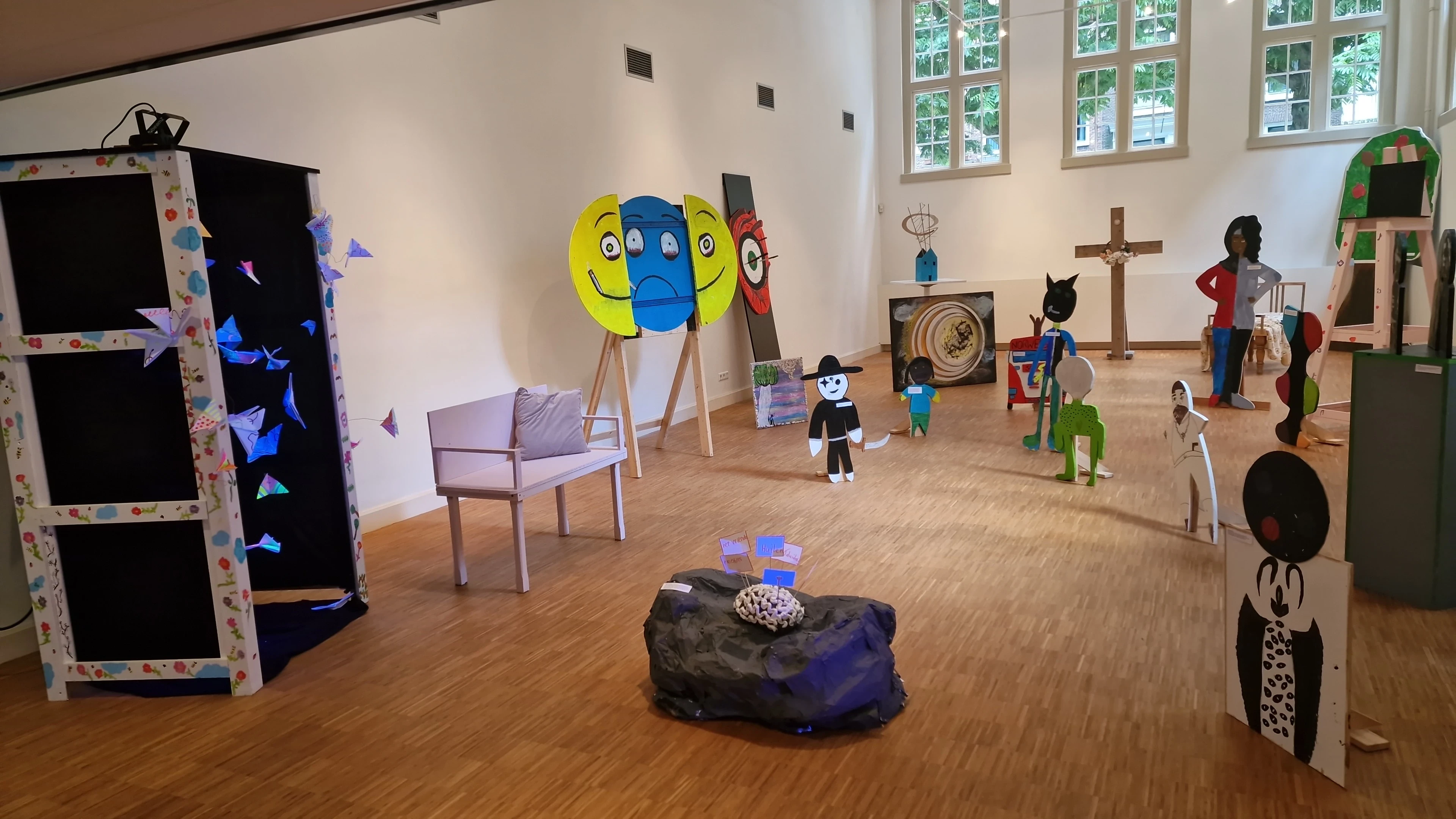 Kunsttentoonstelling met kleurrijke kartonnen figuren en installaties in een lichte ruimte