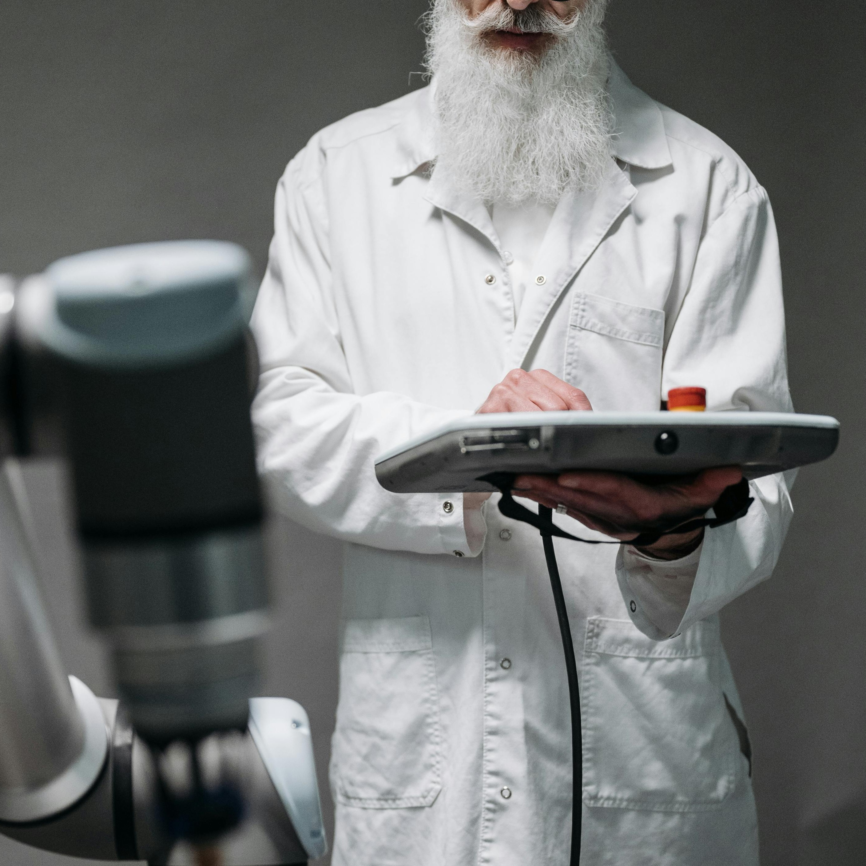 A man holds a robot pendant and uses the touch screen to program it.