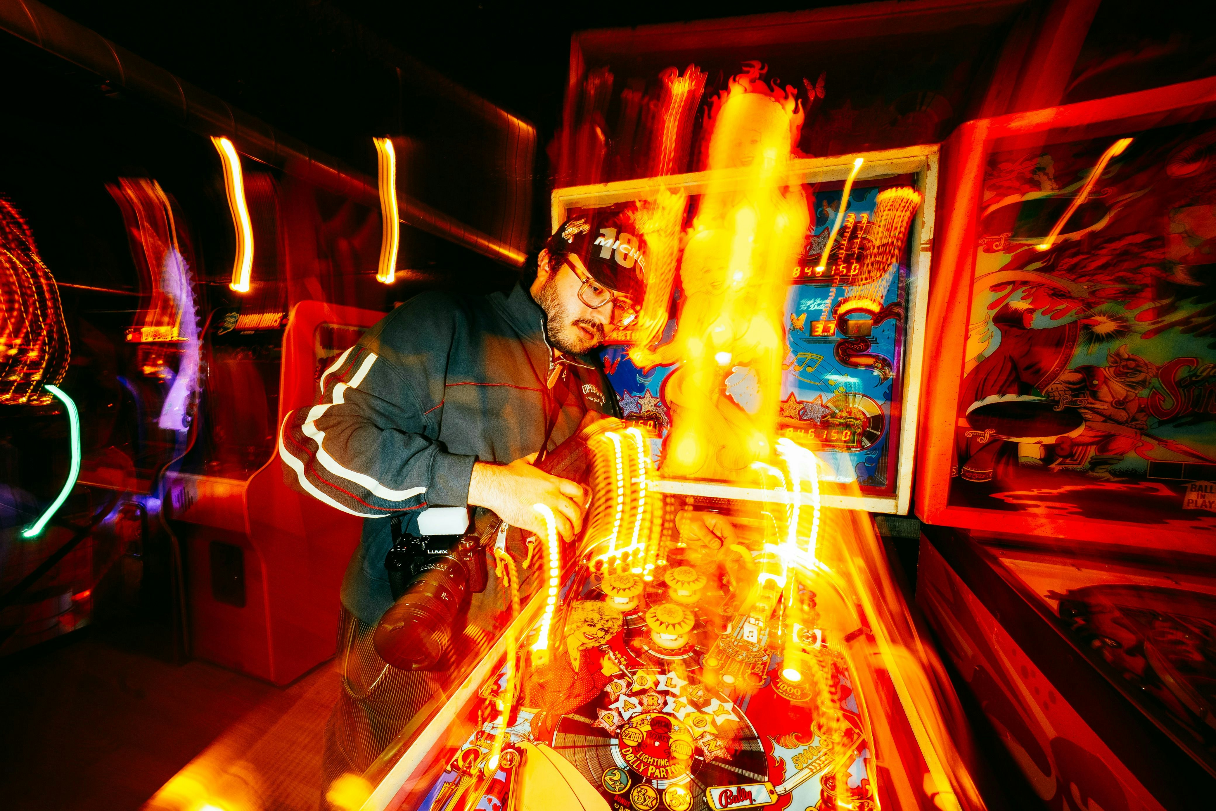 Man playing a brightly lit pinball machine at night