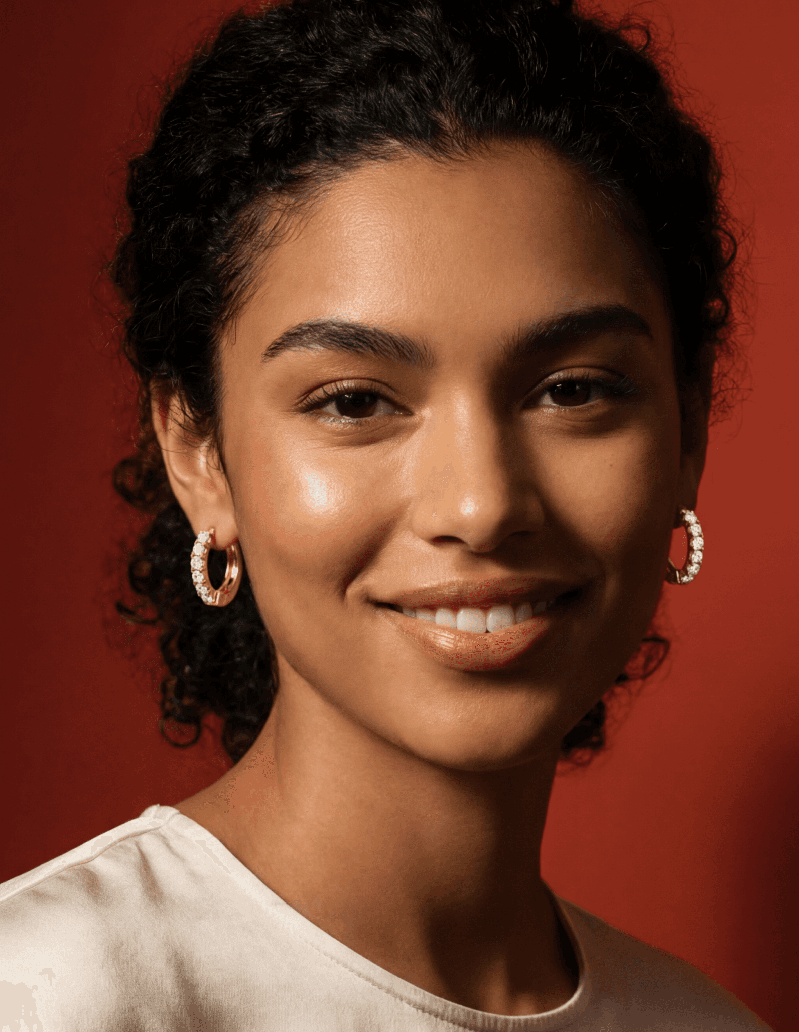 Woman with curly hair wearing gold hoop earrings against a warm studio background