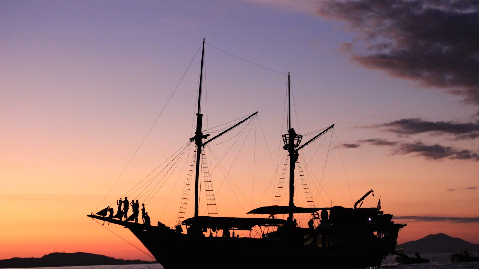 Traditional wooden phinisi liveaboard silhouetted against a sunset in eastern Indonesia