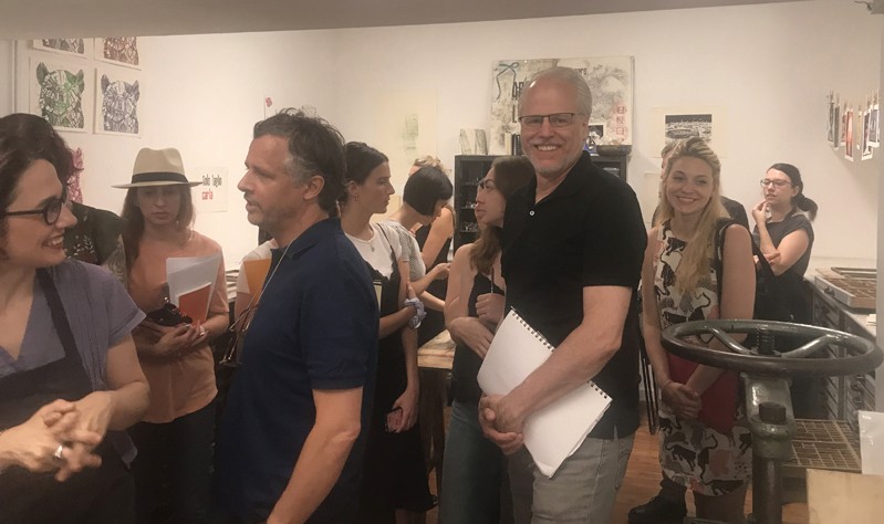A photo of a group of people talking to each other while standing in a printing workshop.