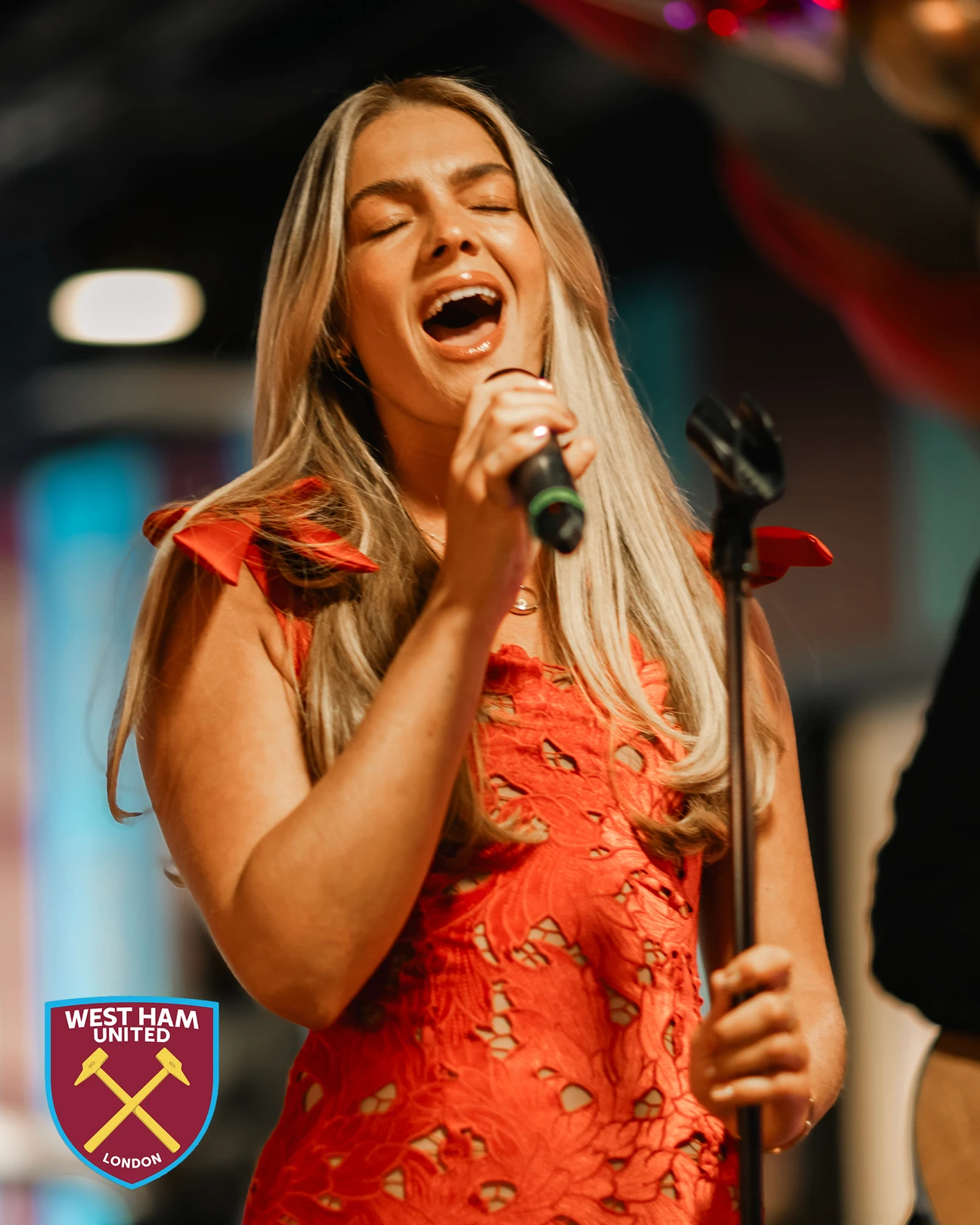 Woman singing into a microphone, West Ham United logo.