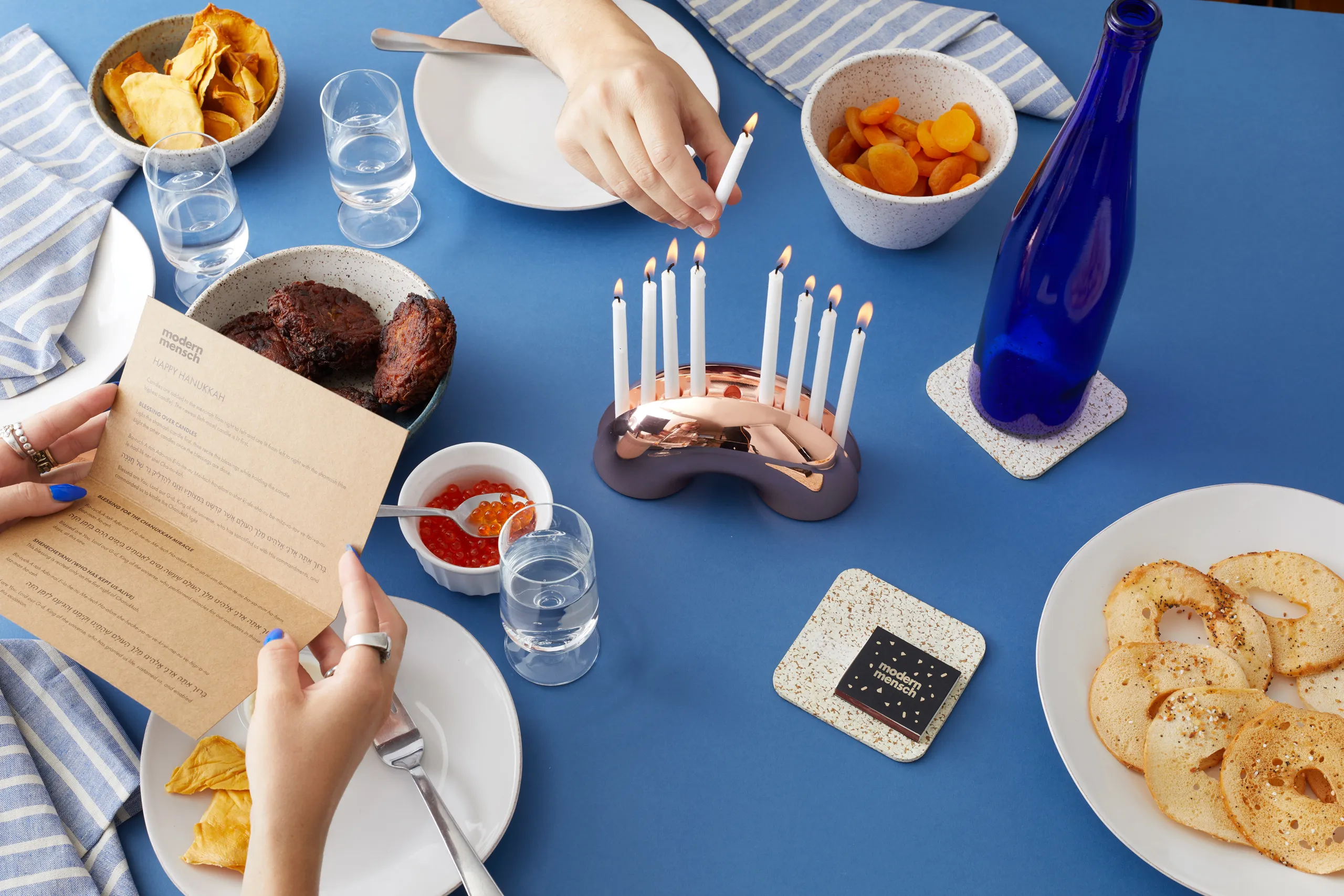 Nosh Menorah centered on a blue dinner table during a Hanukkah meal
