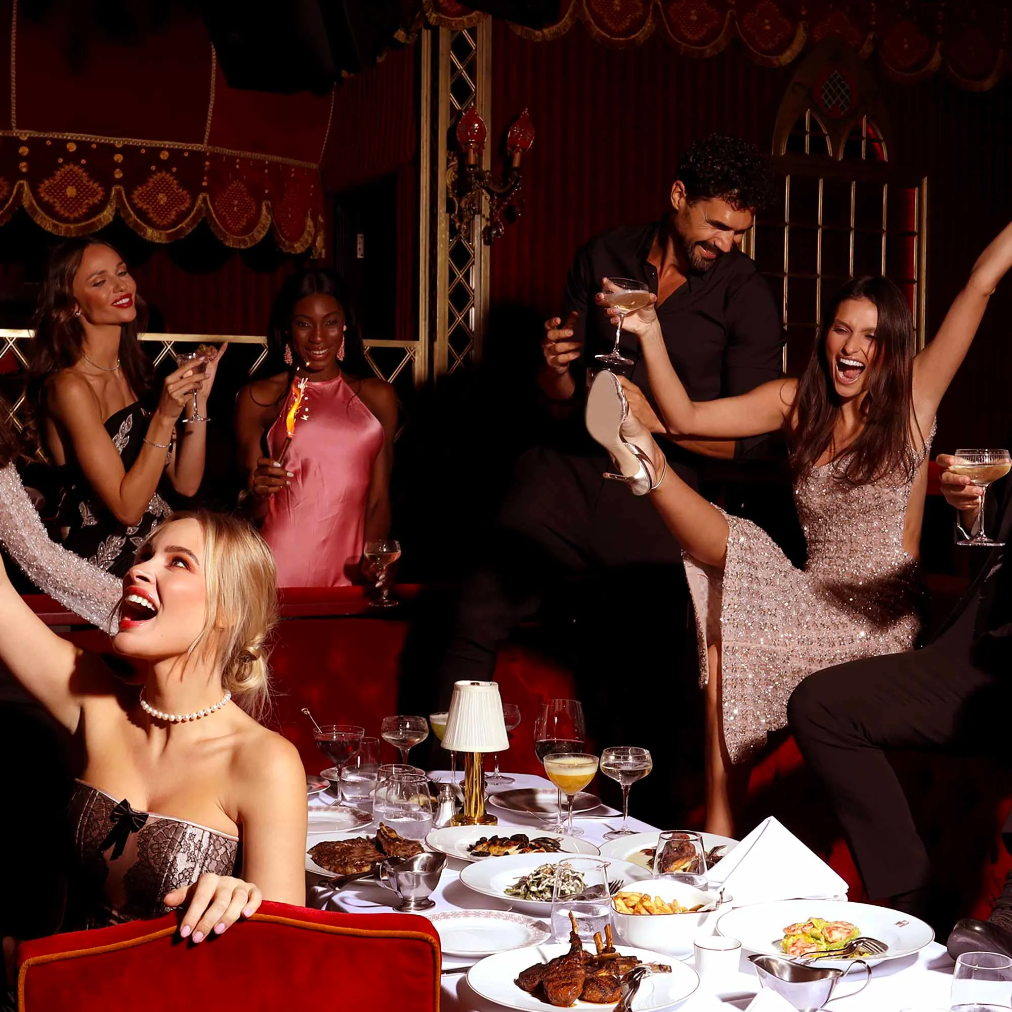 Guests celebrating around a dinner table at Raspoutine Dubai, raising cocktails and a high heel in the air