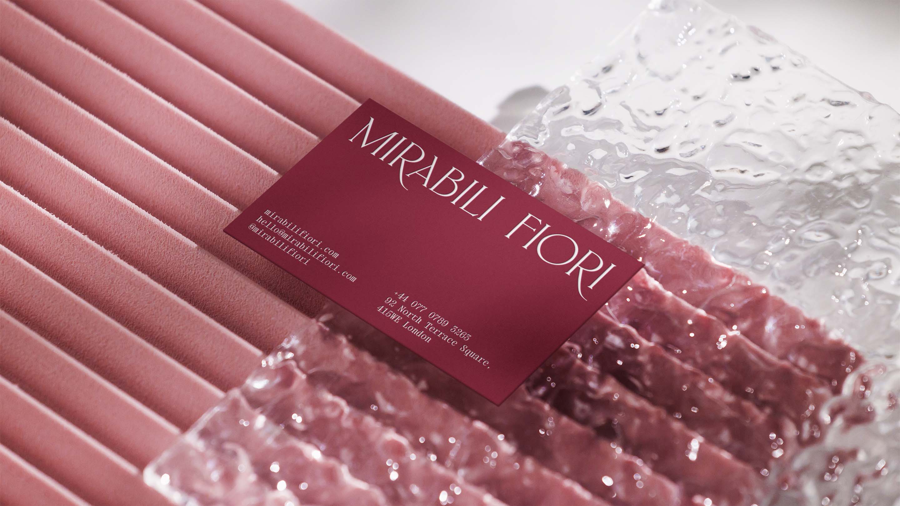 Mirabili Fiori burgundy business card on textured transparent glass surface on pink background