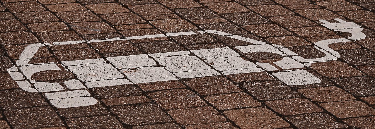 Ein Symbol eines Elektroautos mit Stecker auf einem Parkplatz.