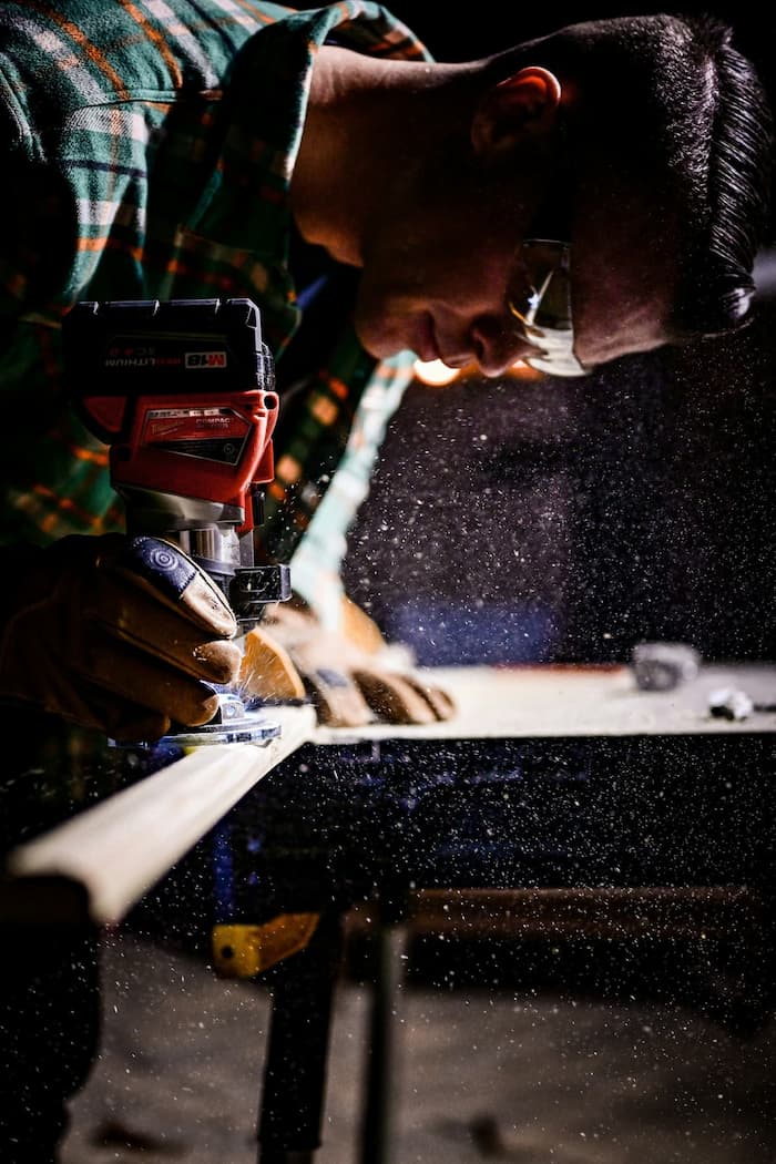Carpenter Using power tool to shape wood while wearing safety goggles and gloves in workshop.