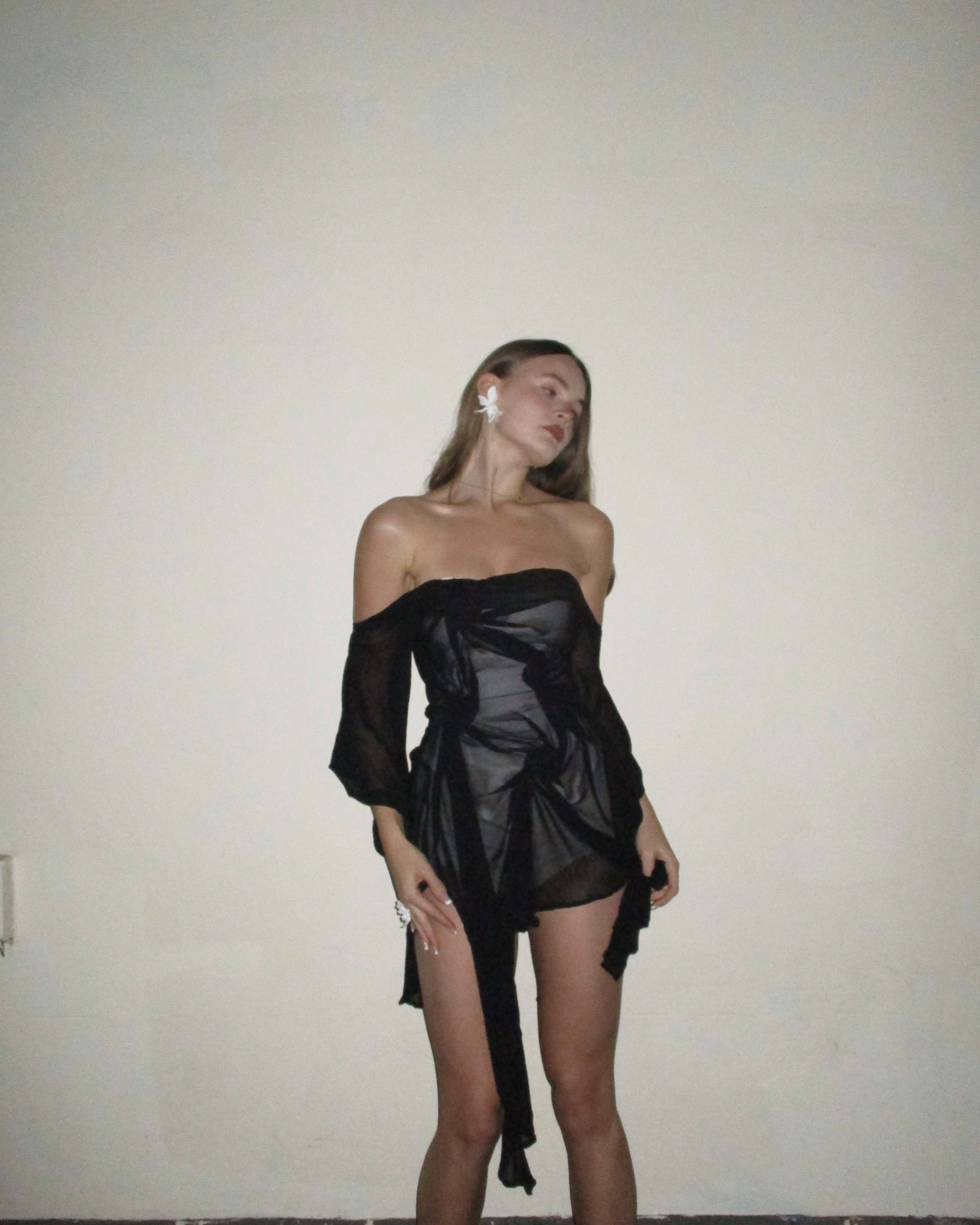 Black sheer off-shoulder dress with soft draped bodice, semi-transparent fabric, and fluid mid-length skirt