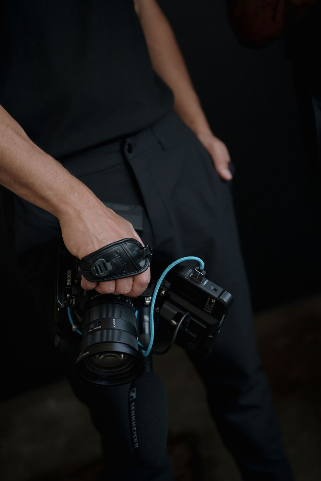 A person's hand holds a gaming controller while wearing black clothing in a dimly lit setting.