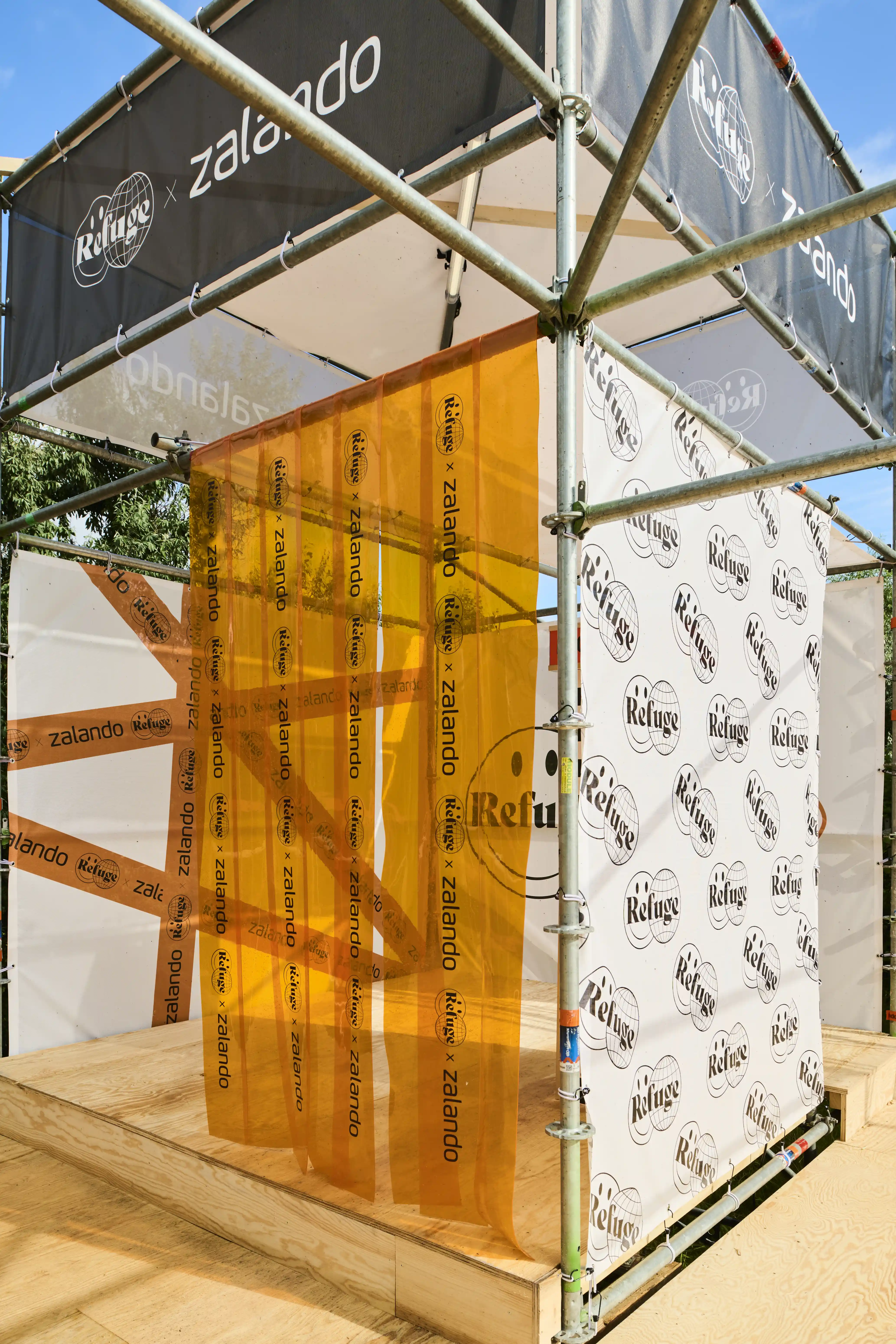 Scaffold cube with orange sheer curtain, Refuge pattern banner and Zalando branding.