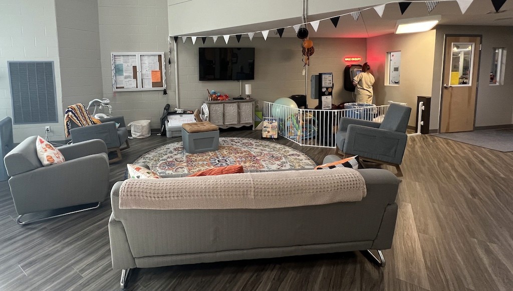 The nursery living area features couches with blankets draped over them, a flat-screen TV and a variety of toys. In the corner, women can use a kiosk to place commissary orders. A “Male on Duty” sign above the kiosk alerts the unit that male correctional officers are nearby.