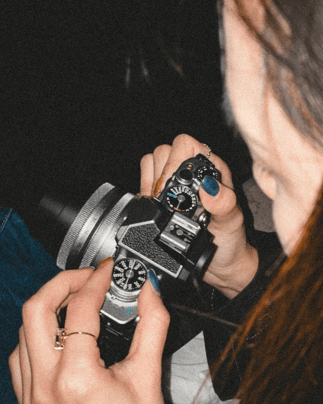 A close-up of a person's hands adjusting the dials on a retro-style mirrorless camera in dark lighting
