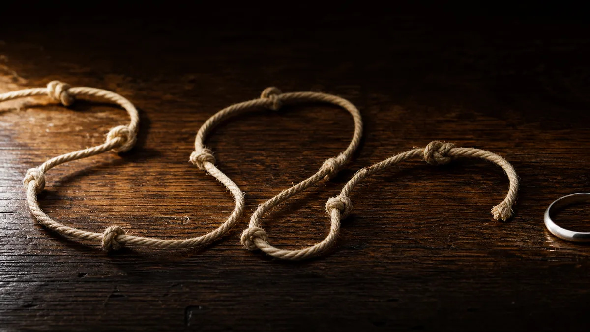 An old knotted cotton cord and a plain metal ring on dark walnut under narrow warm light